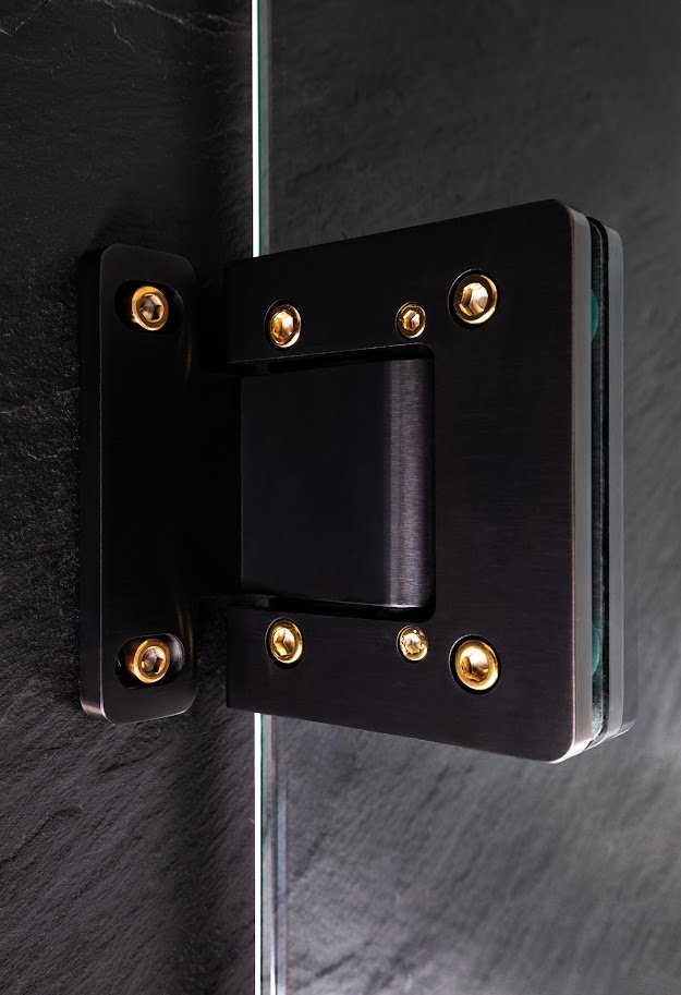 Close-up of a black metal wall mount bracket with gold screws, attached to dark tiled wall.