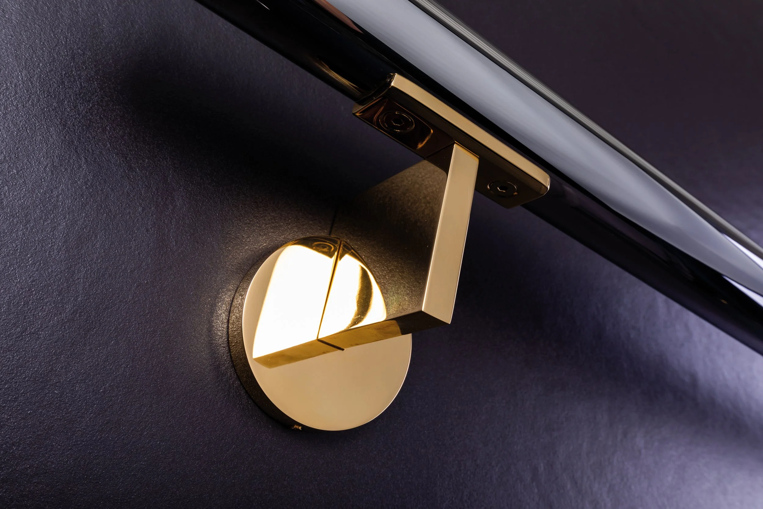 Close-up of a modern gold and black wall-mounted light fixture with a rectangular design, installed on a dark wall, partially illuminating the surface.