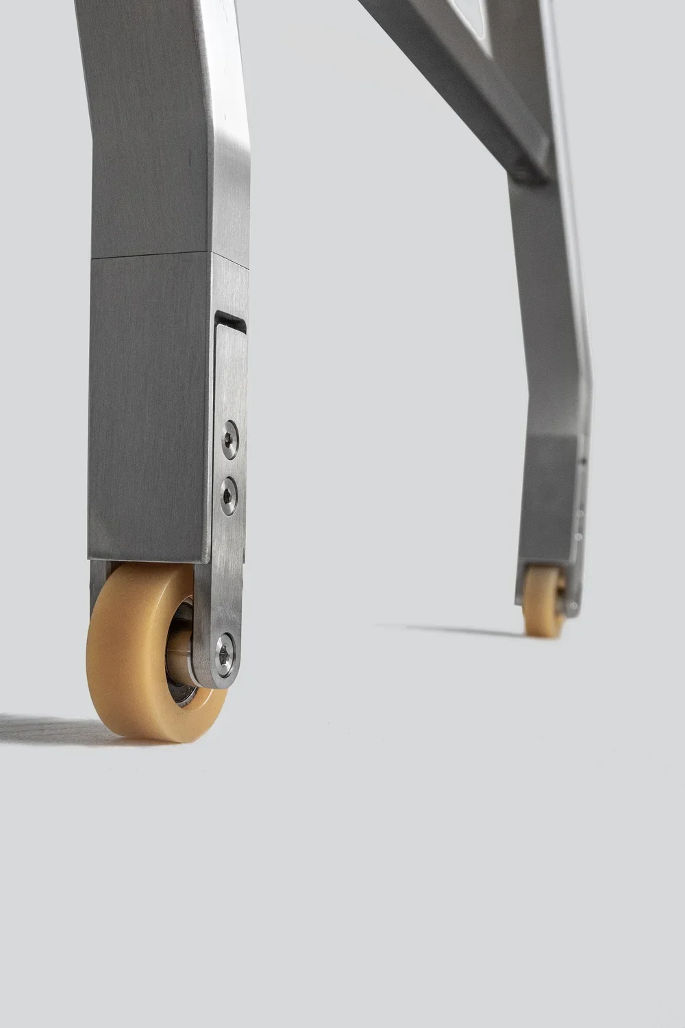 Close-up of a metal frame with beige caster wheels on a light gray background.