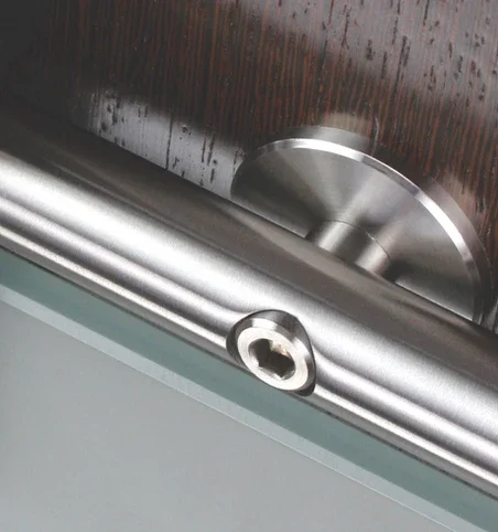 Close-up of a metallic door closer with a circular hinge and a small visible screw, mounted on a wooden door.