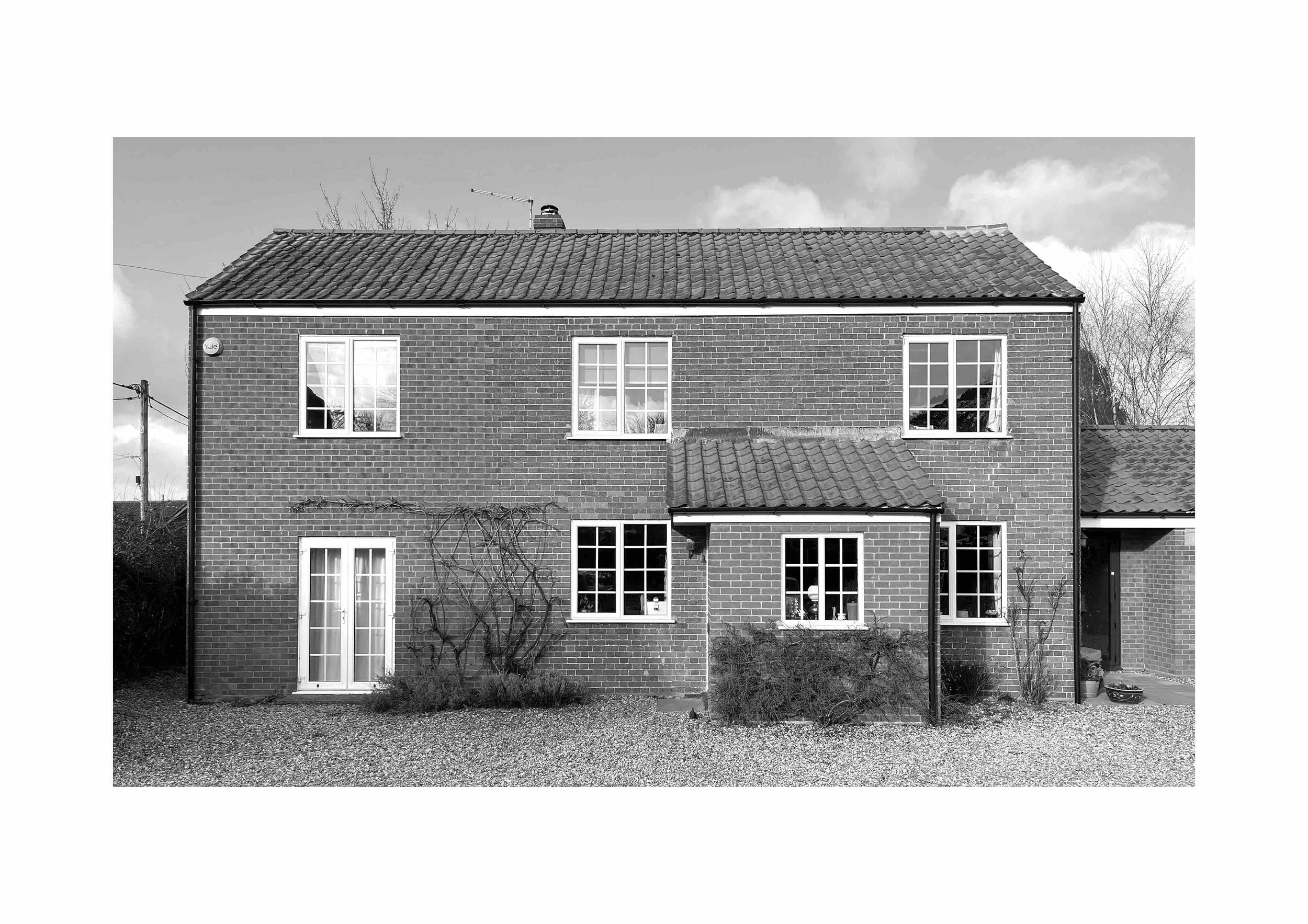 Black and white photo of a two-story brick house with several windows and a tiled roof.