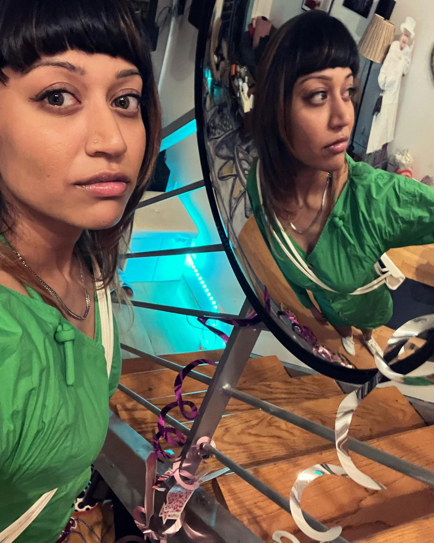 Woman in green dress looking into a mirror with reflection, standing on wooden staircase decorated with ribbons.