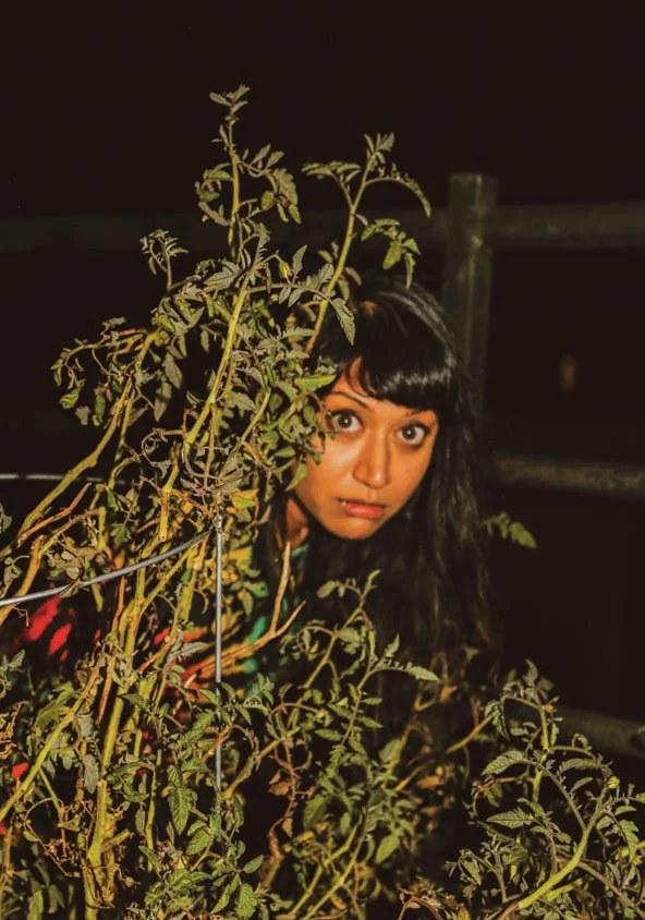 Person with dark hair peeking through tall green plants at night