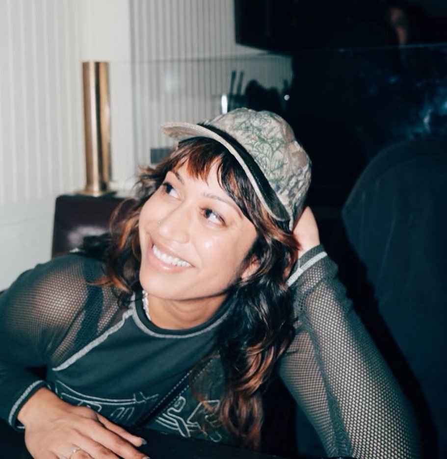 Smiling person in a mesh shirt and cap sitting indoors.