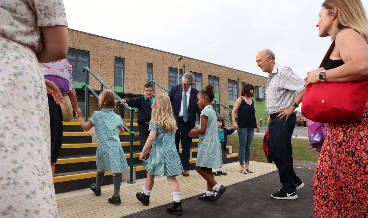 Group of children and adults gathered outside a school building, with children wearing school uniforms.