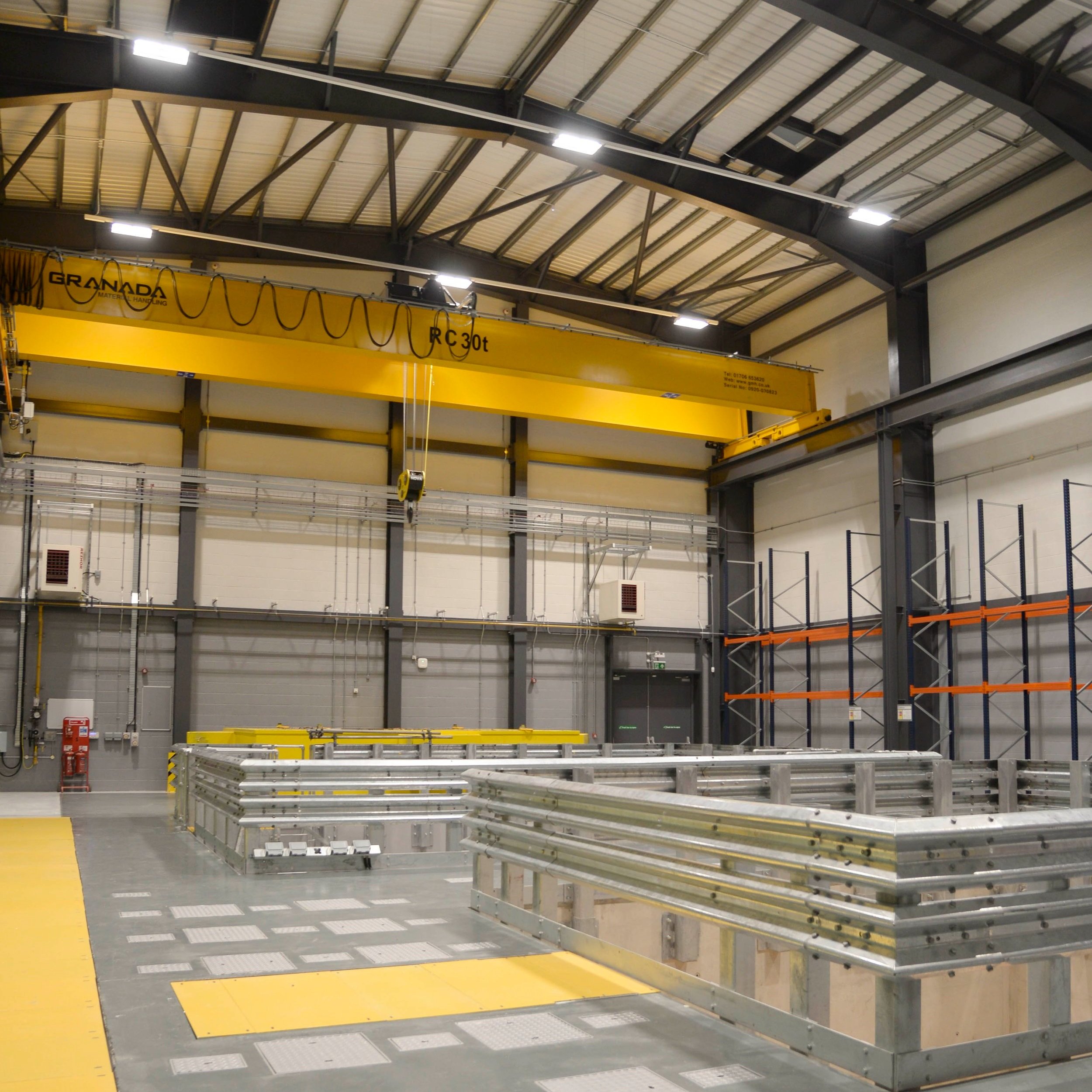 Large industrial warehouse interior with yellow overhead crane, metal structures, and storage racks.