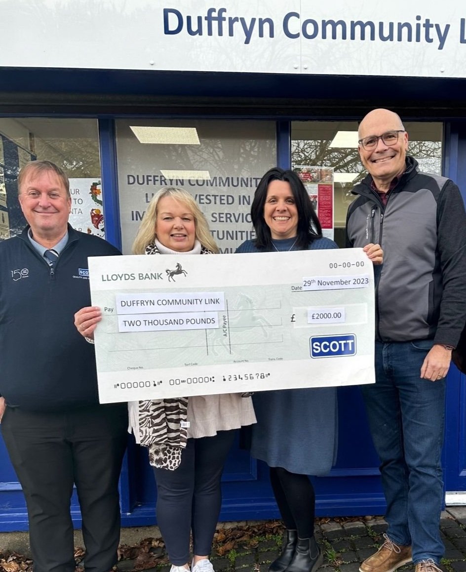 Four people standing outside in front of a community center holding a large ceremonial check for two thousand pounds from Lloyds Bank to Dufryn Community Link, dated November 29, 2023.
