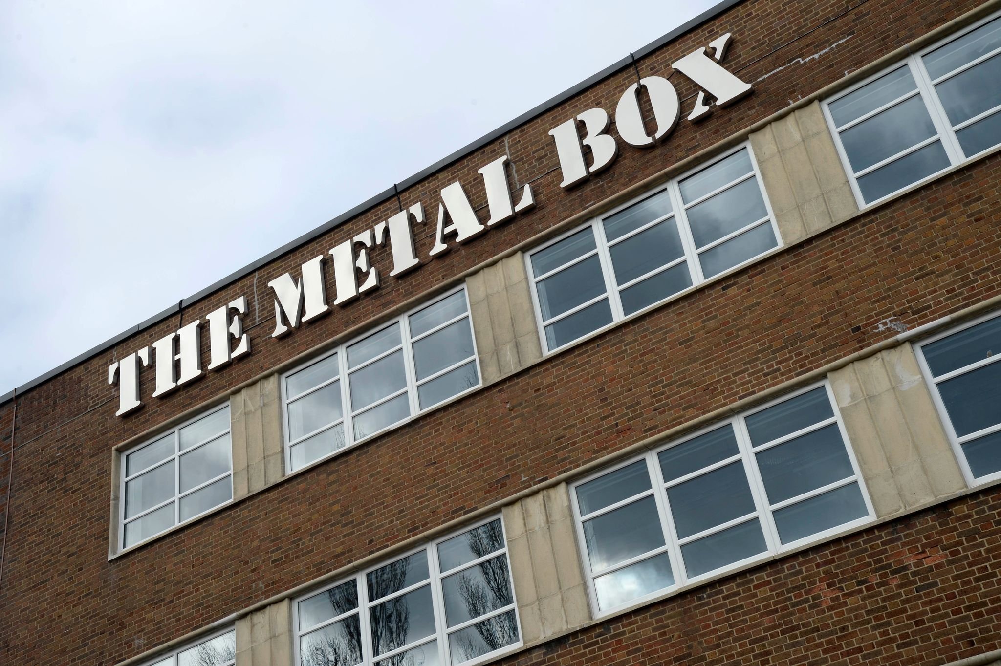 Brick building with 'The Metal Box' sign and large windows.