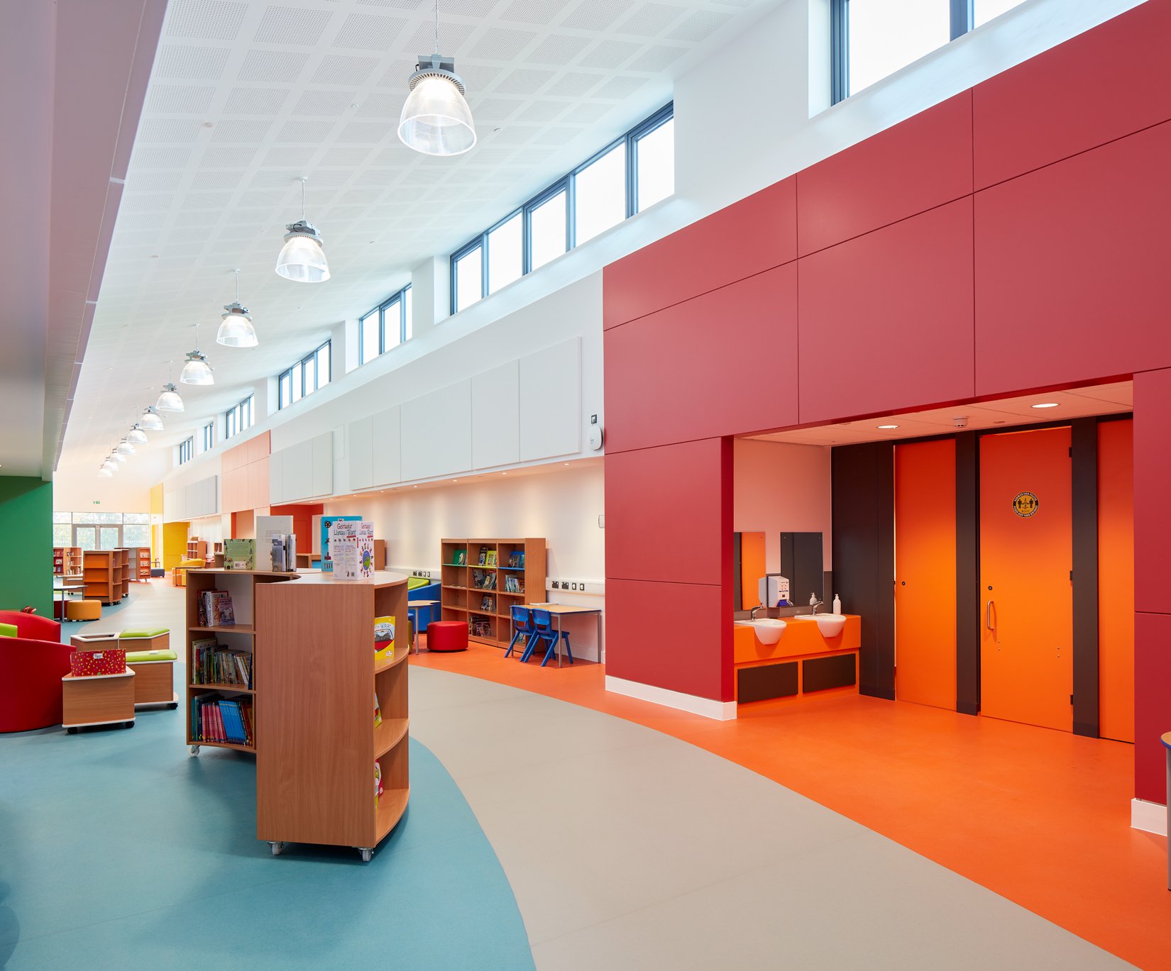 Interior of a modern colorful library with children's section, bookshelves, and seating area, featuring red, blue, and orange walls and fixtures.