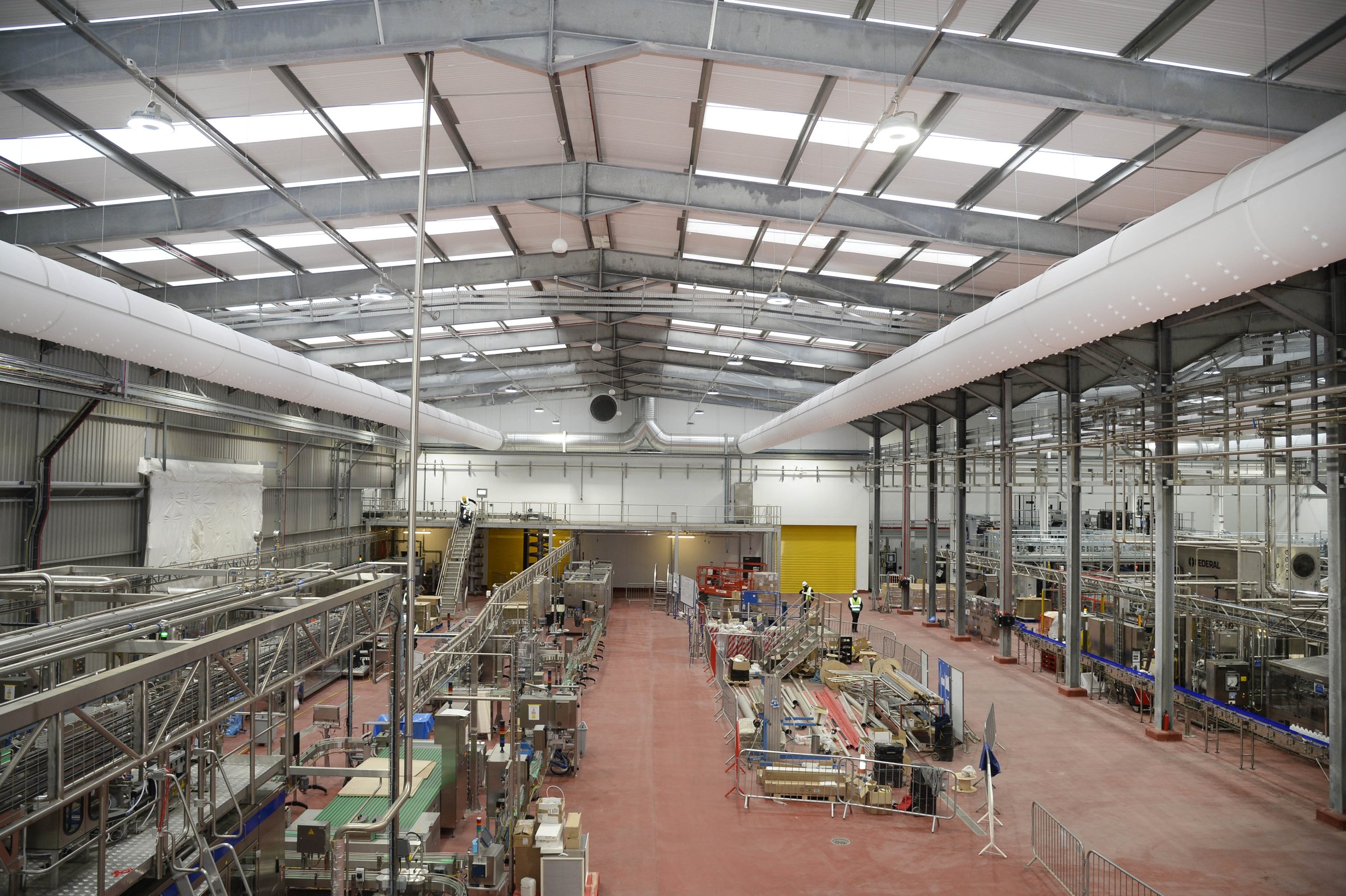 Interior of a large industrial warehouse with various machinery, conveyor belts, and workers in safety vests.