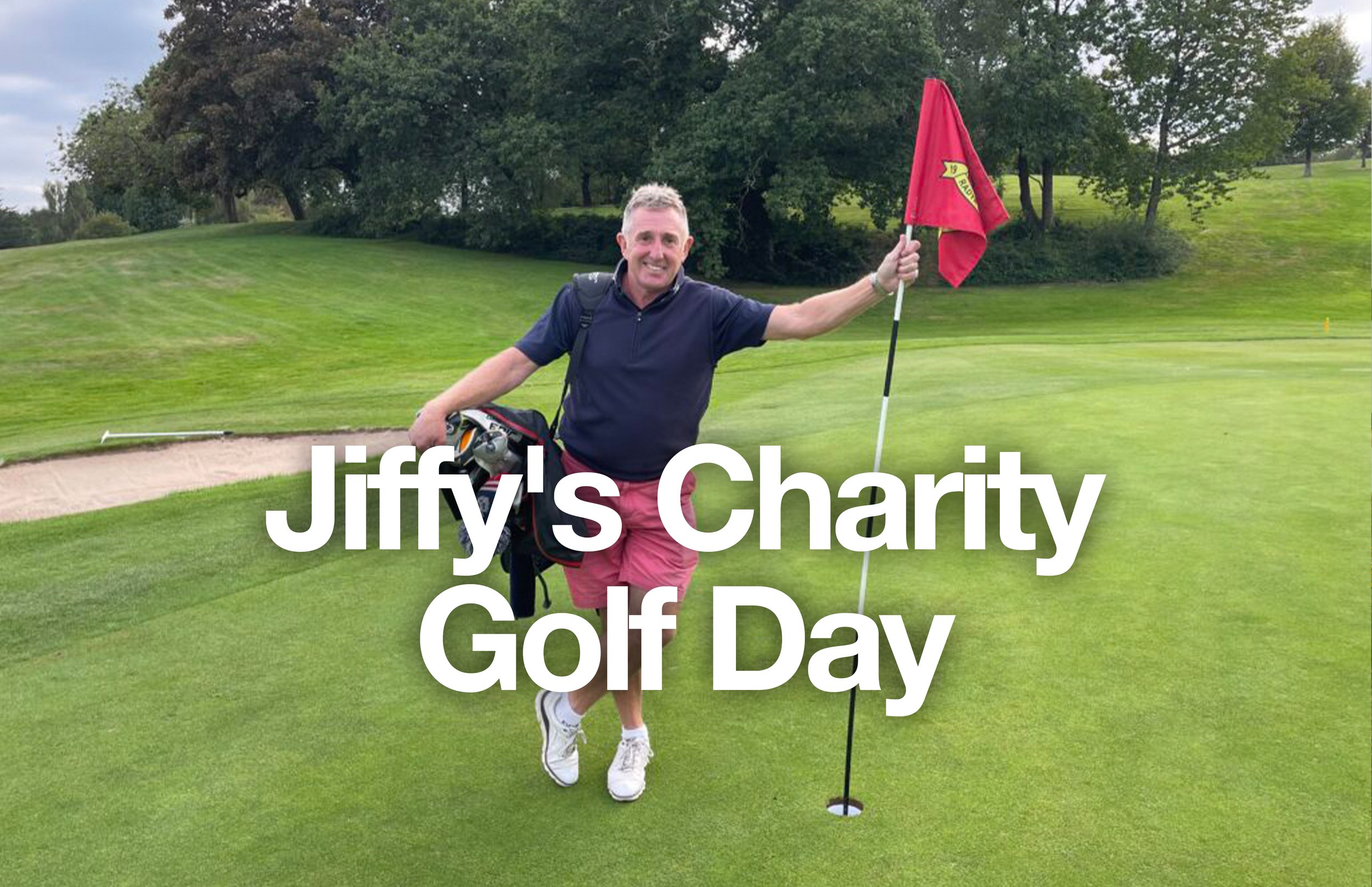 Man standing on golf course holding a golf flag, smiling, with golf bag and trees in background, celebrating Jiffy's Charity Golf Day.