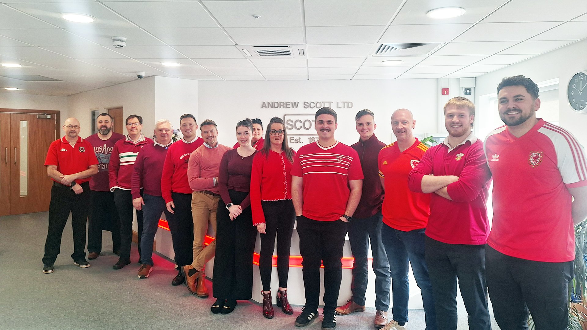 Group of people wearing red standing in an office with a sign that reads 'Andrew Scott Ltd.'