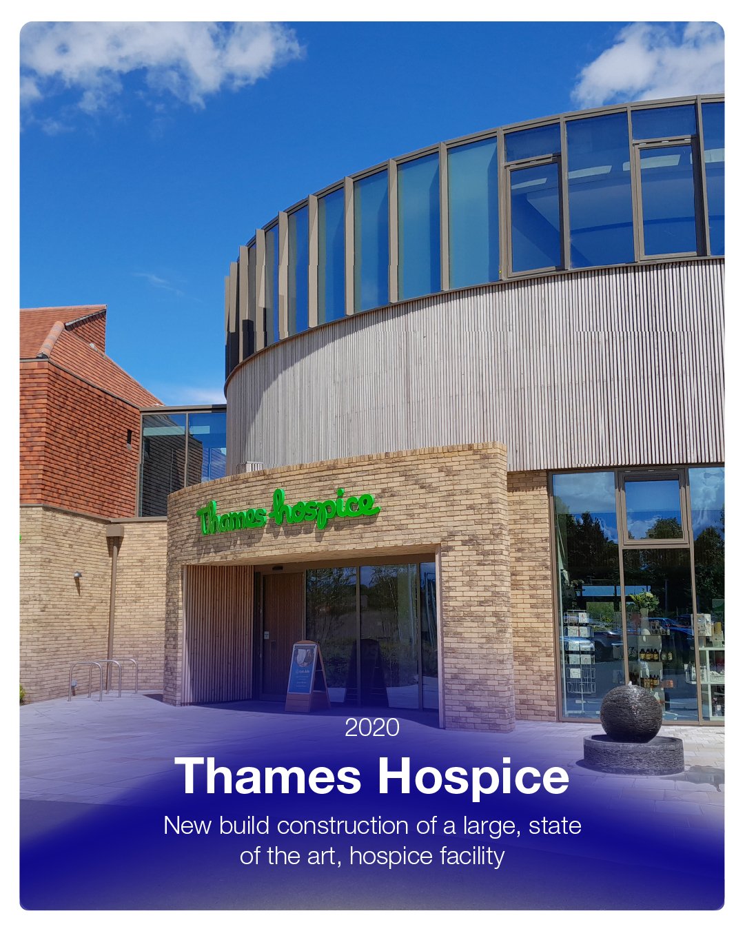 Front view of Thames Hospice building with brick and metal exterior, large glass windows, and green neon sign, under a blue sky with scattered clouds.