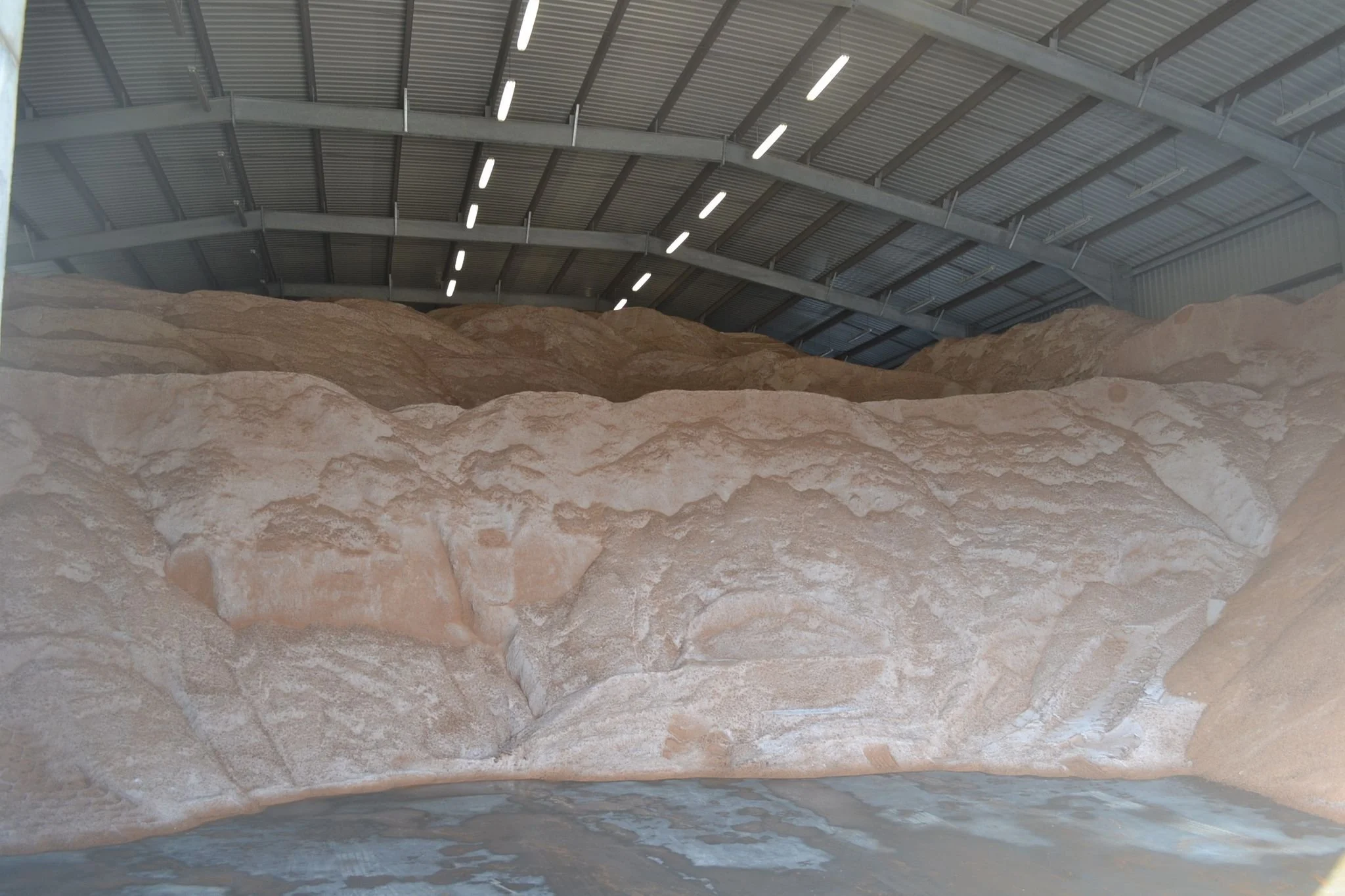 Artificial indoor salt cave with large salt rocks and a body of water at the bottom under a high metal roof.
