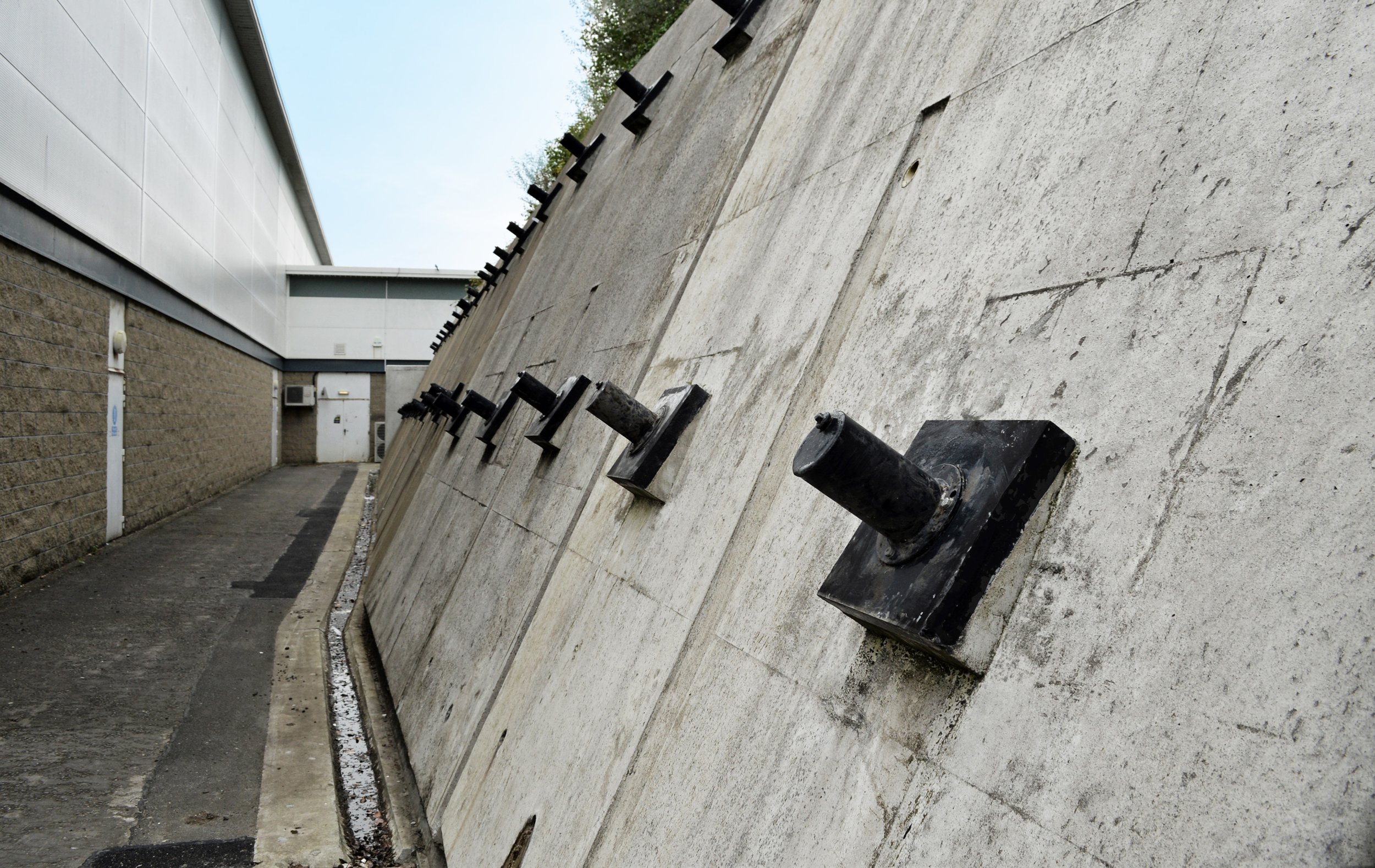 Industrial building exterior with sloped retaining wall and black drainage pipes