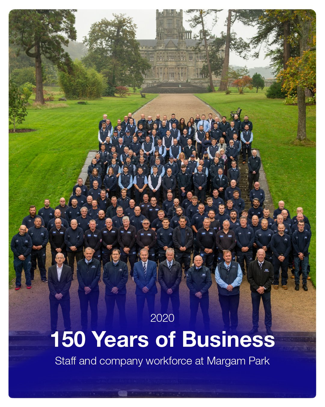 A large group of staff and company employees posed for a group photo on steps outdoors at Margam Park with a historic castle in the background, celebrating 150 years of business in 2020.