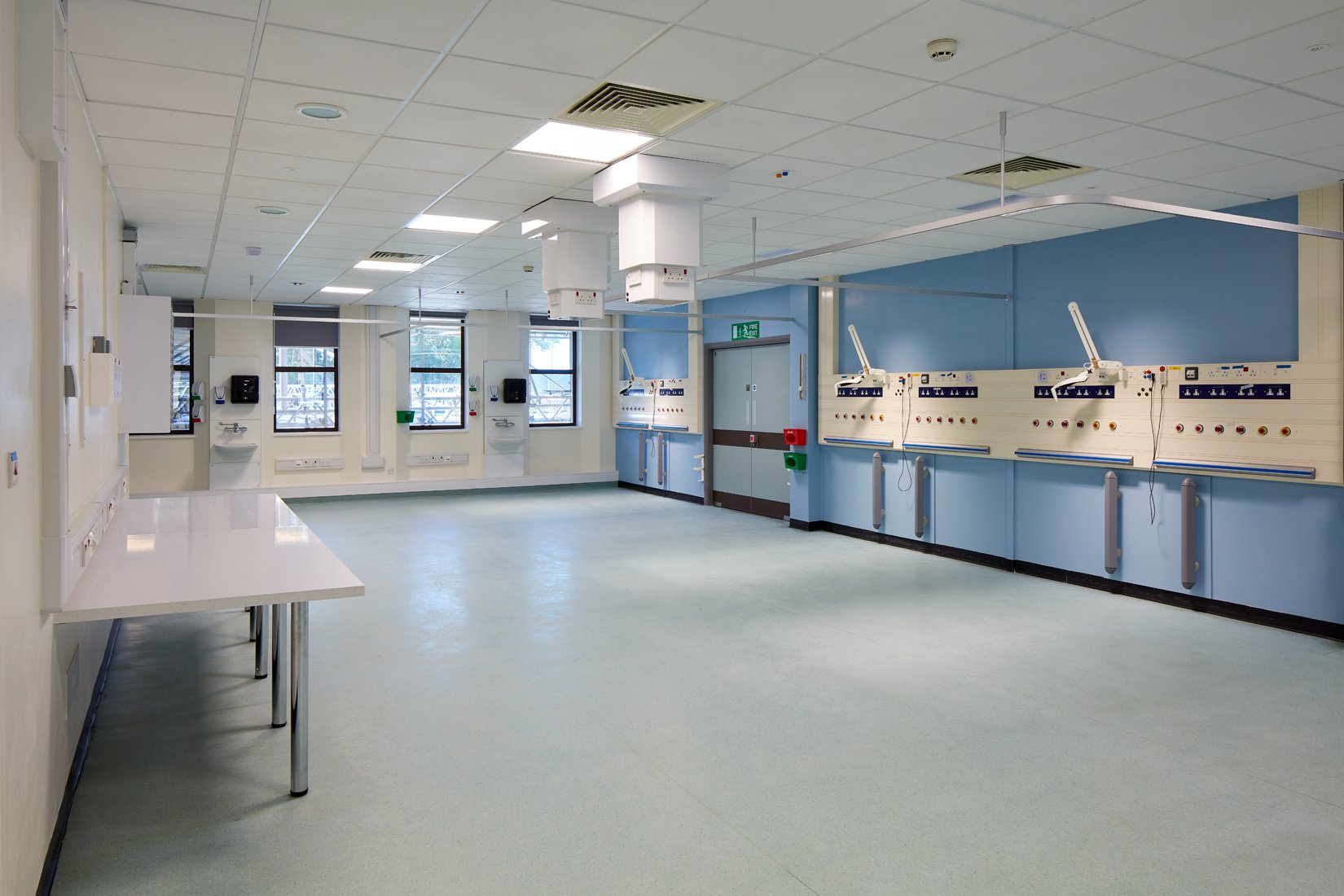Empty hospital room with blue walls, multiple medical gas outlets, and patient beds in the background.