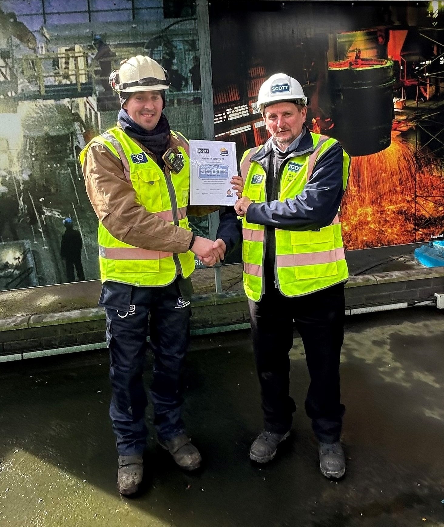 Two men in safety vests and helmets shaking hands, one holding a certificate, with a construction-themed backdrop.