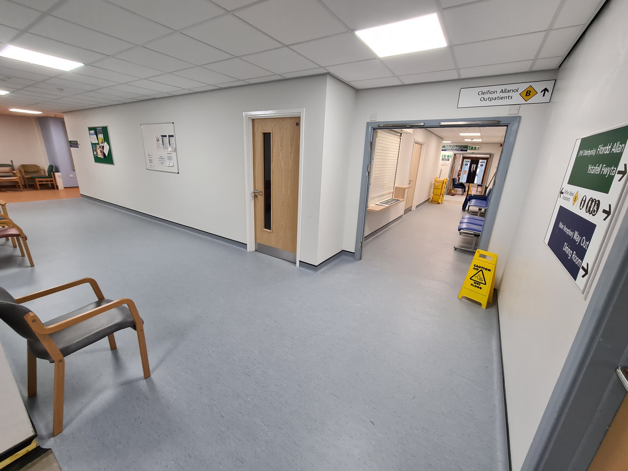 Interior of a hospital corridor with chairs, signs, and a wet floor caution sign.