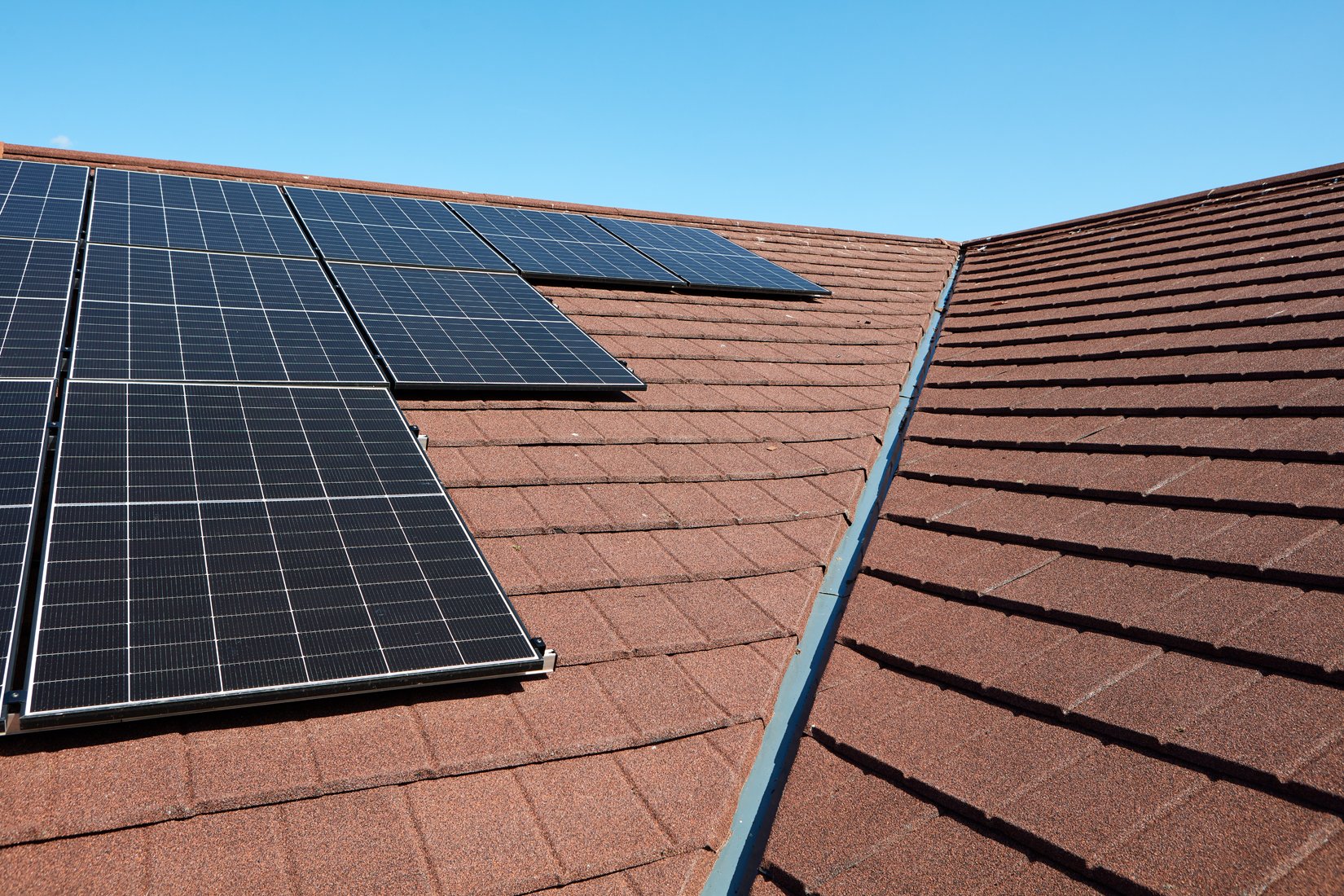 Close-up view of solar panels installed on a red shingled rooftop under a clear blue sky.