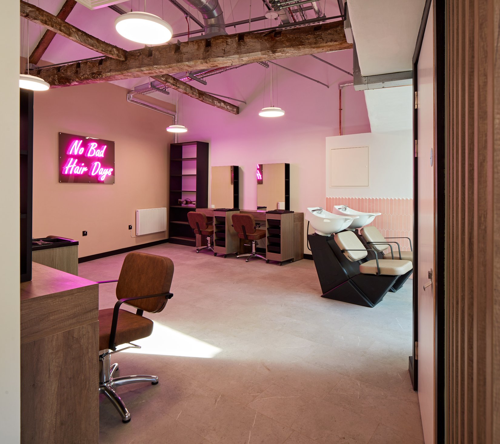 Modern hair salon interior with styling chairs, mirrors, and wash basins; features a neon sign reading 'No Bad Hair Days' on the wall.