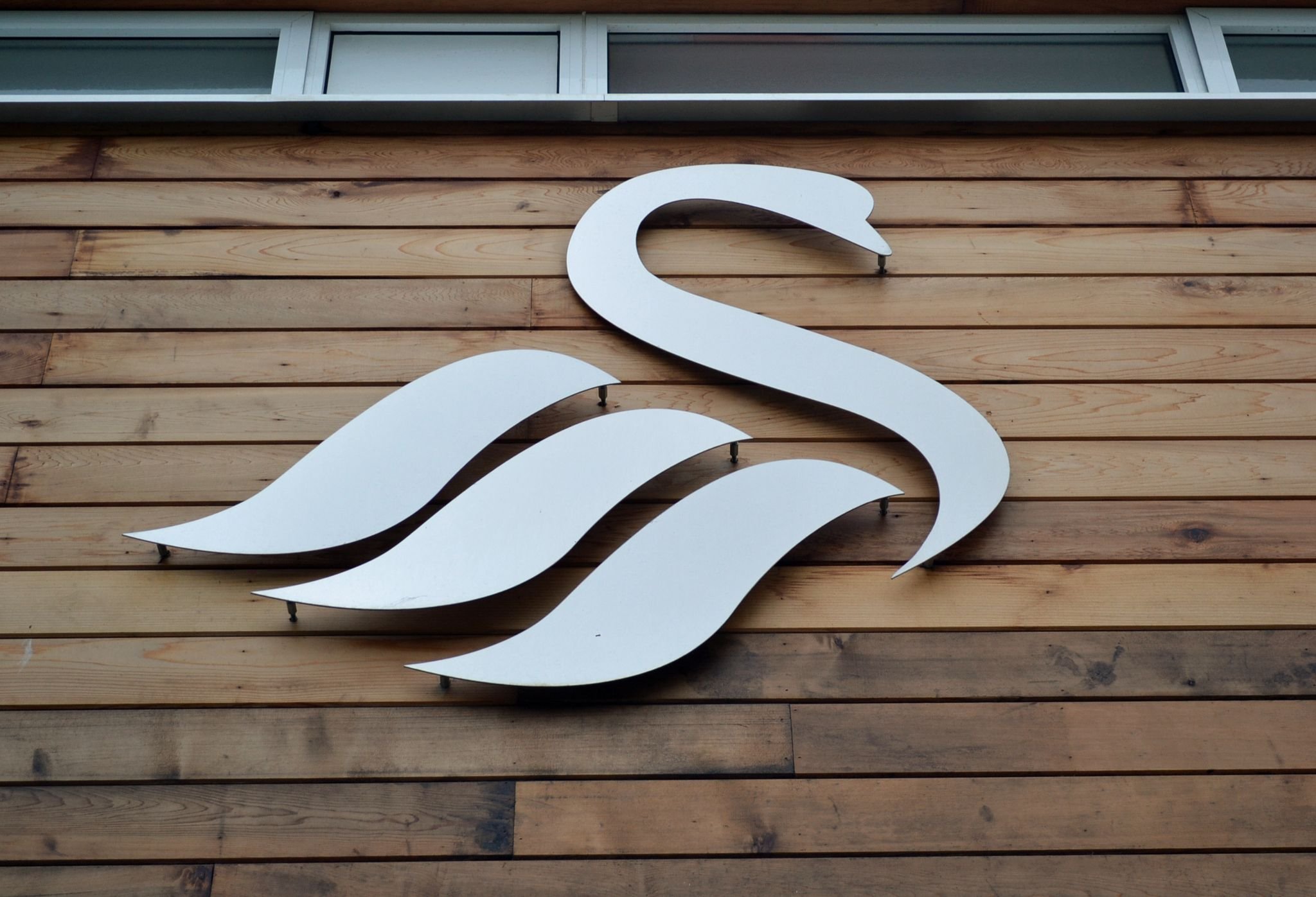 Metal swan logo on wooden wall