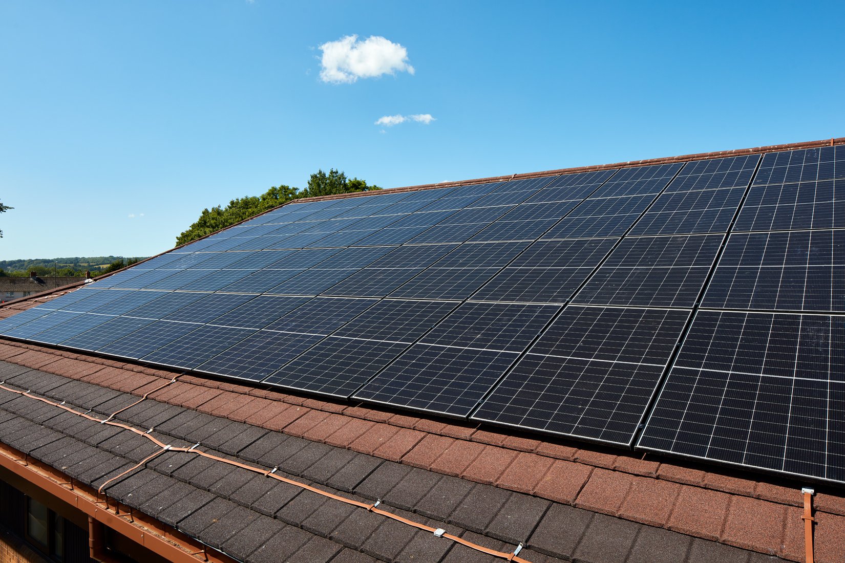 Solar panels installed on a rooftop under a clear blue sky with a few white clouds.