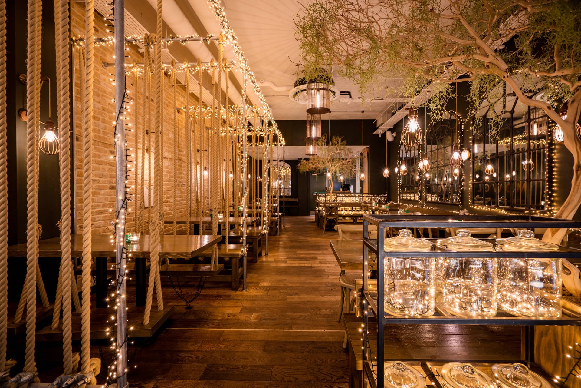 Interior of a restaurant with hanging lights, rope decorations, and wooden furnishings, creating a cozy atmosphere.