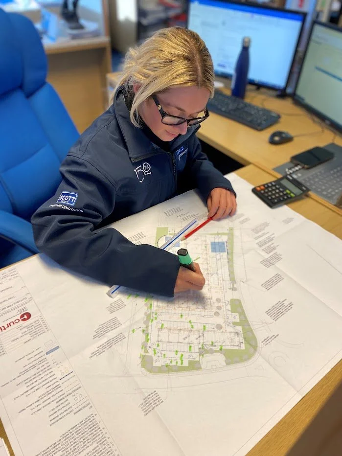Woman with blonde hair and glasses working on a detailed landscape plan at a desk with multiple computer screens.