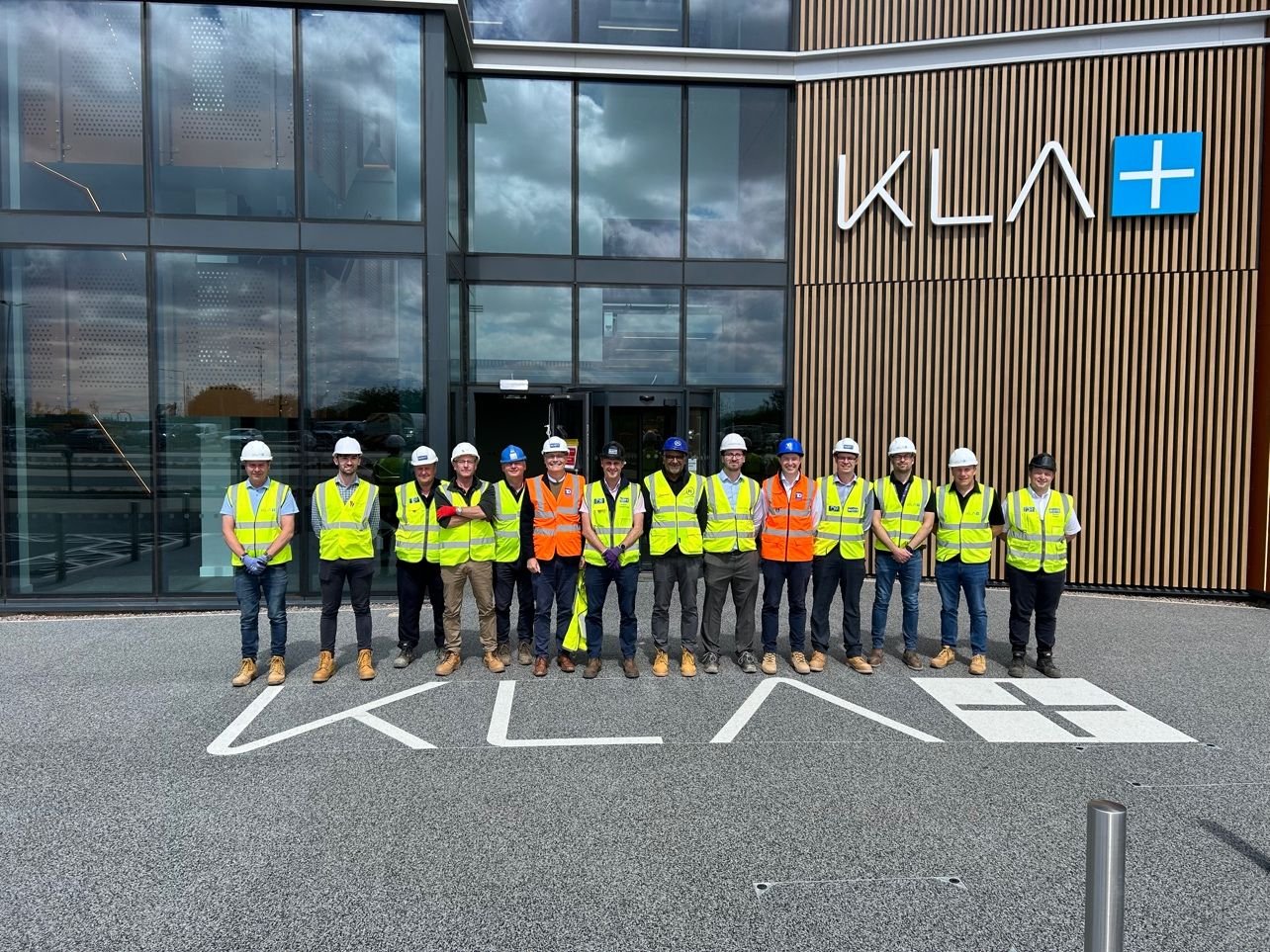 Group of people wearing hard hats and reflective vests standing in front of a building with KLA logo