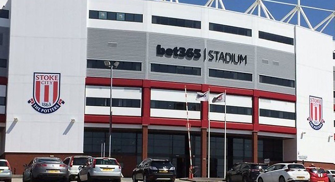 Exterior view of Bet365 Stadium, home of Stoke City Football Club, featuring the club's emblem on the building and several parked cars.