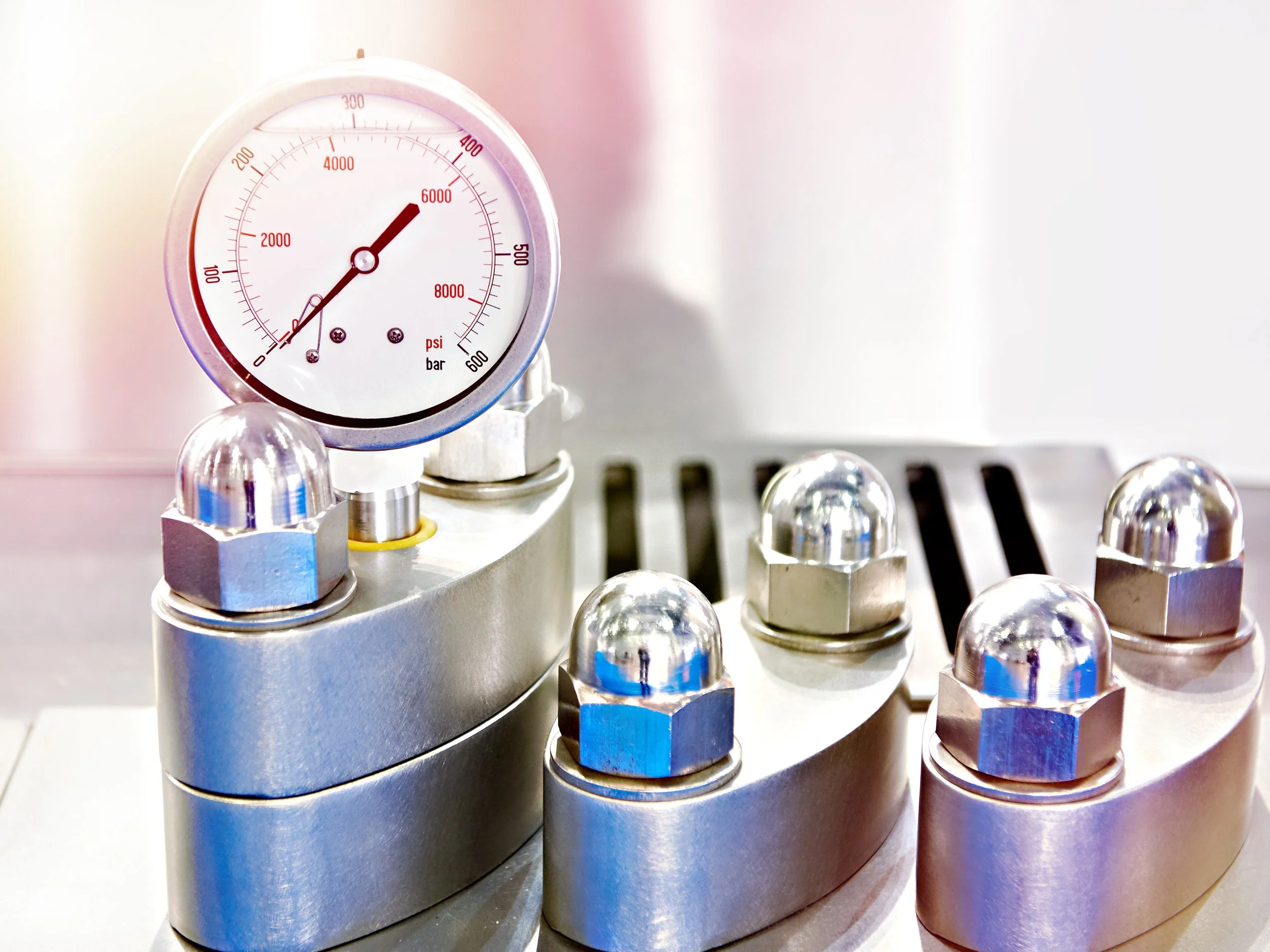 Close-up of a metal industrial pressure gauge and control valves, with a white background.