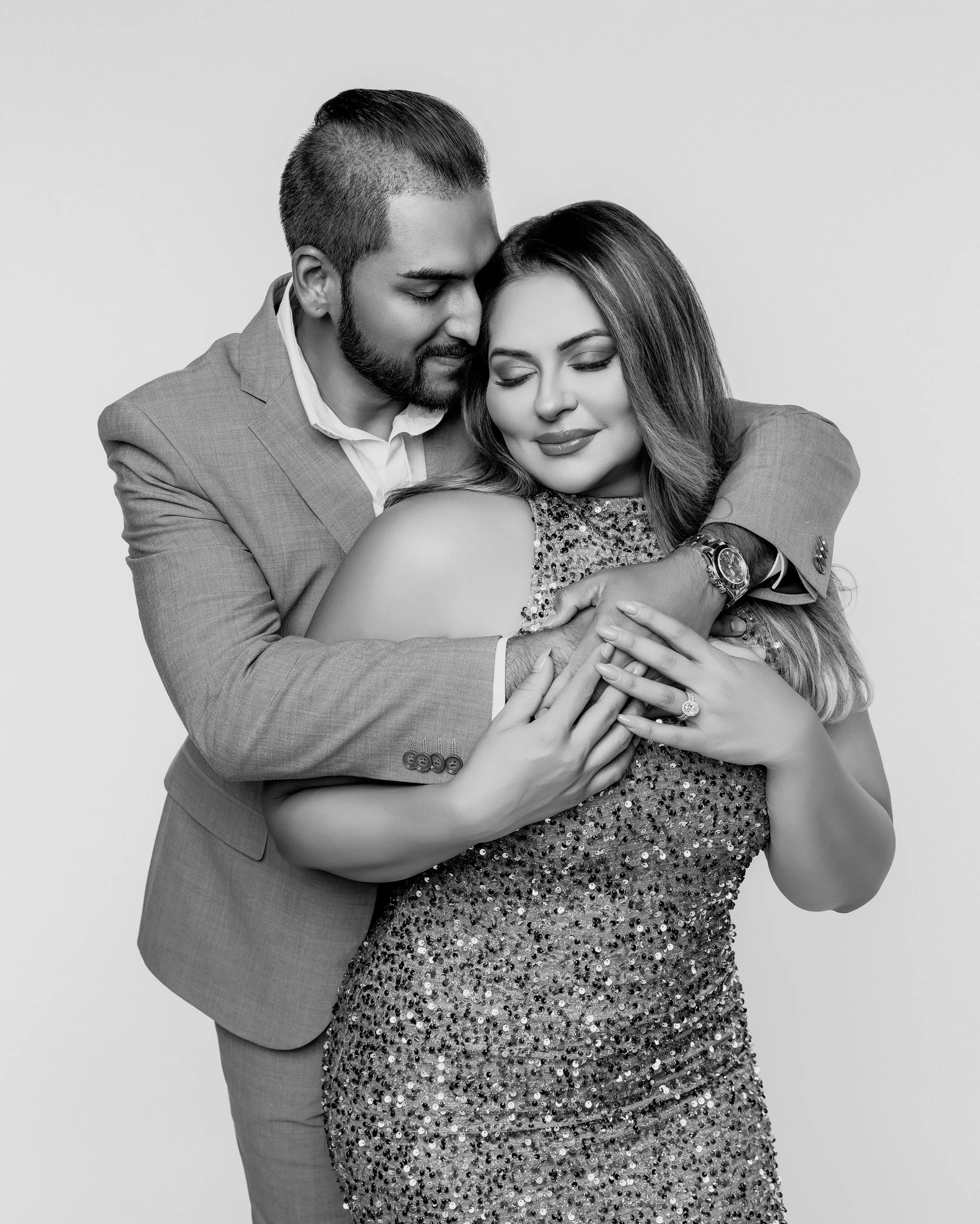 A couple embracing, with eyes closed, smiling, in black and white. The man is in a suit, the woman in a sequined dress.