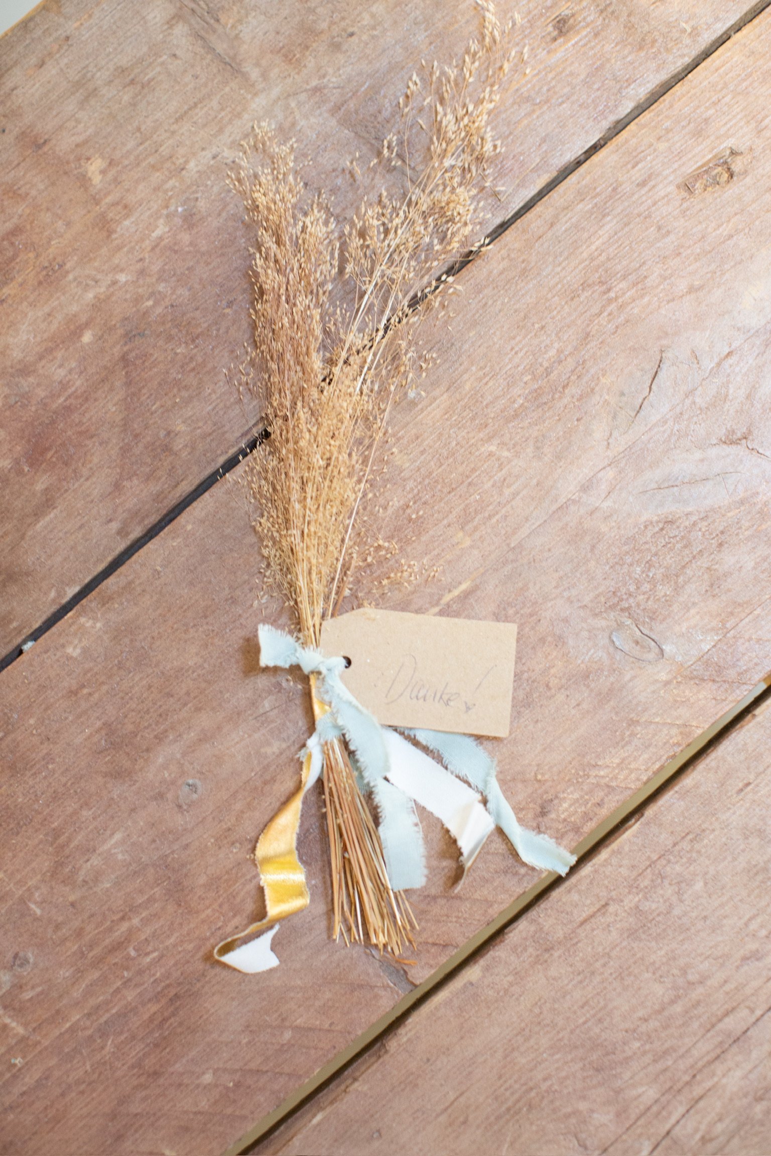 Kleine getrocknete Maiskolben mit Bändern und einem handgeschriebenen Dankes-Kärtchen auf einem Holztisch.
