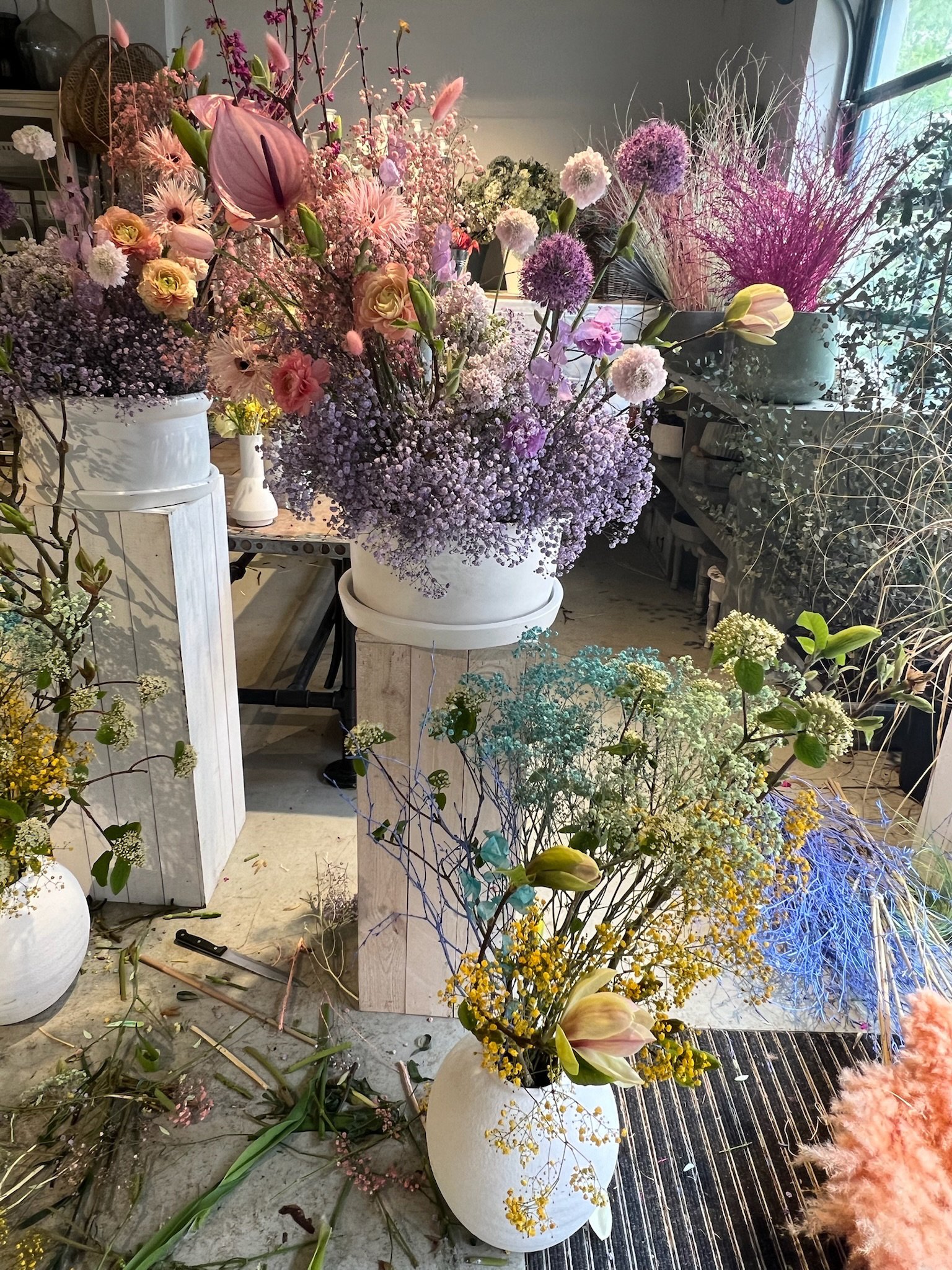 Bunte große und kleine Blumenarrangements in weißen und grauen Vasen in einem Blumenatelier.