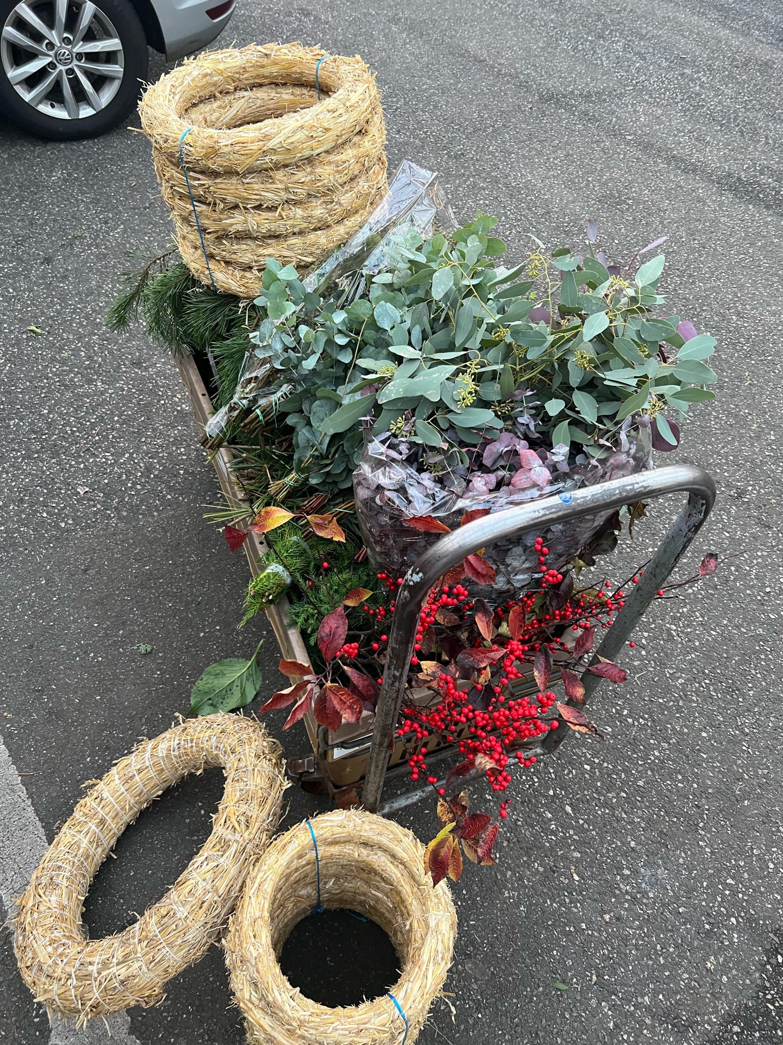 Ein Einkaufswagen voller Weihnachtsdekoration, including Tannenzweige, Eukalyptus, rote Beeren, und Strohringe.
