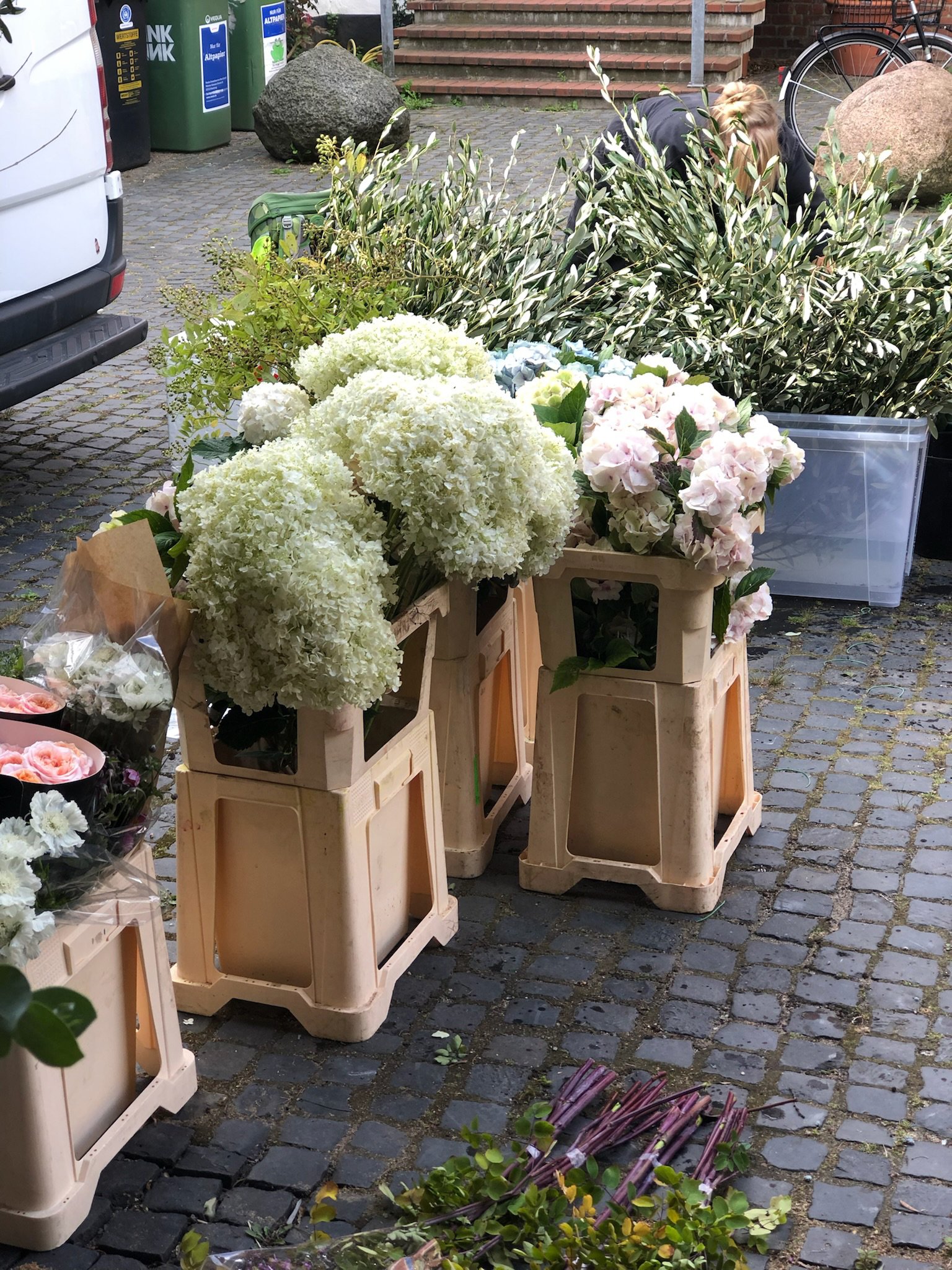 Blumenstand mit weißen und pastellfarbenen Blumen auf Paletten in einer Fußgängerzone.