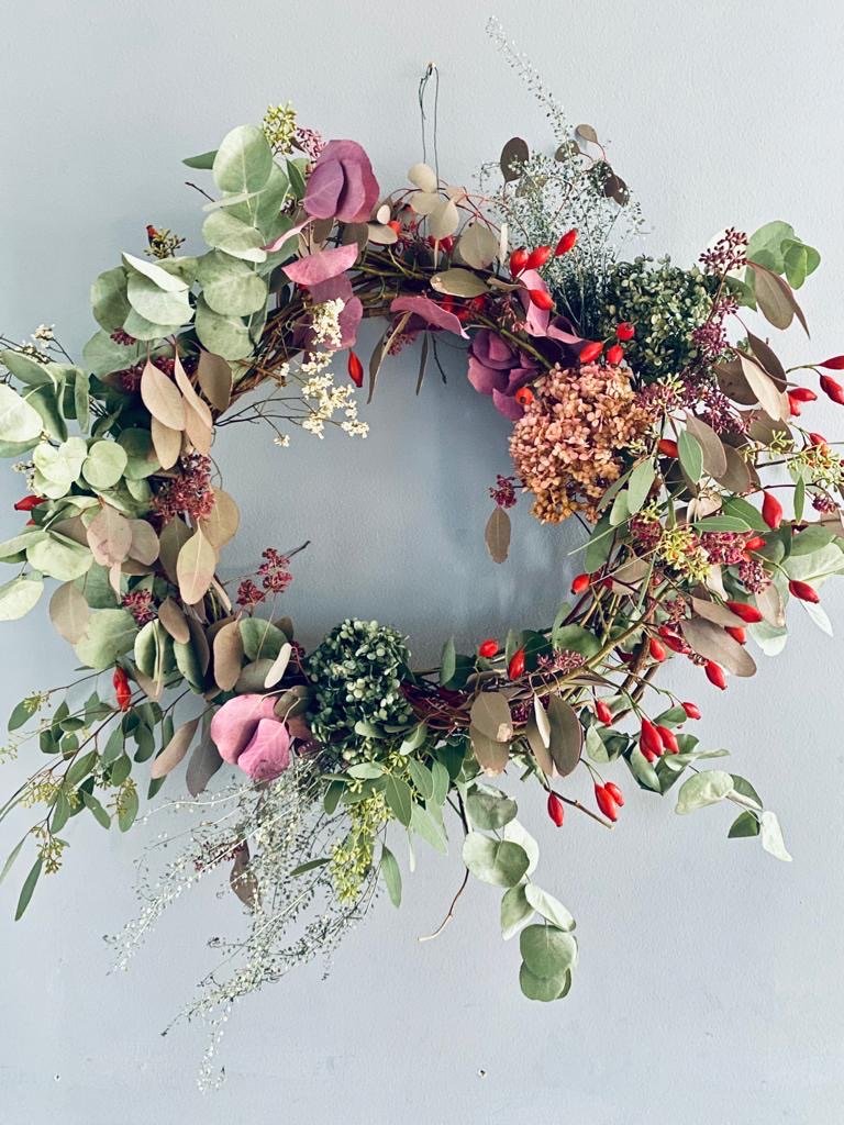 Blumenkranz mit Eukalyptus, Hortensien, roten Beeren und anderen Trockengewächsen an einer weißen Wand