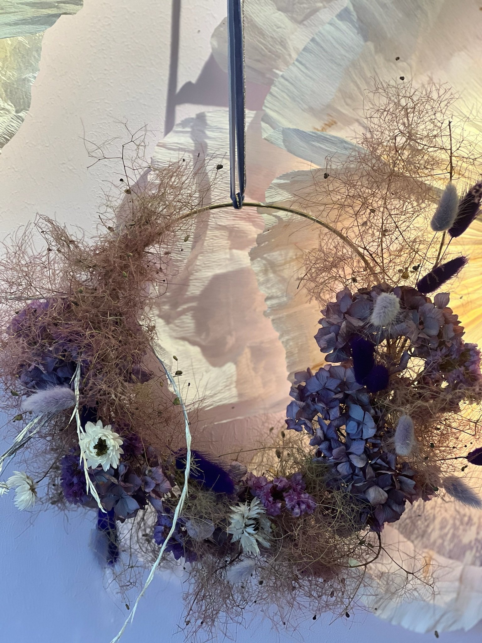 Blumenkranz mit getrockneten Blumen und Gräsern, aufgehängt an einer Wand
