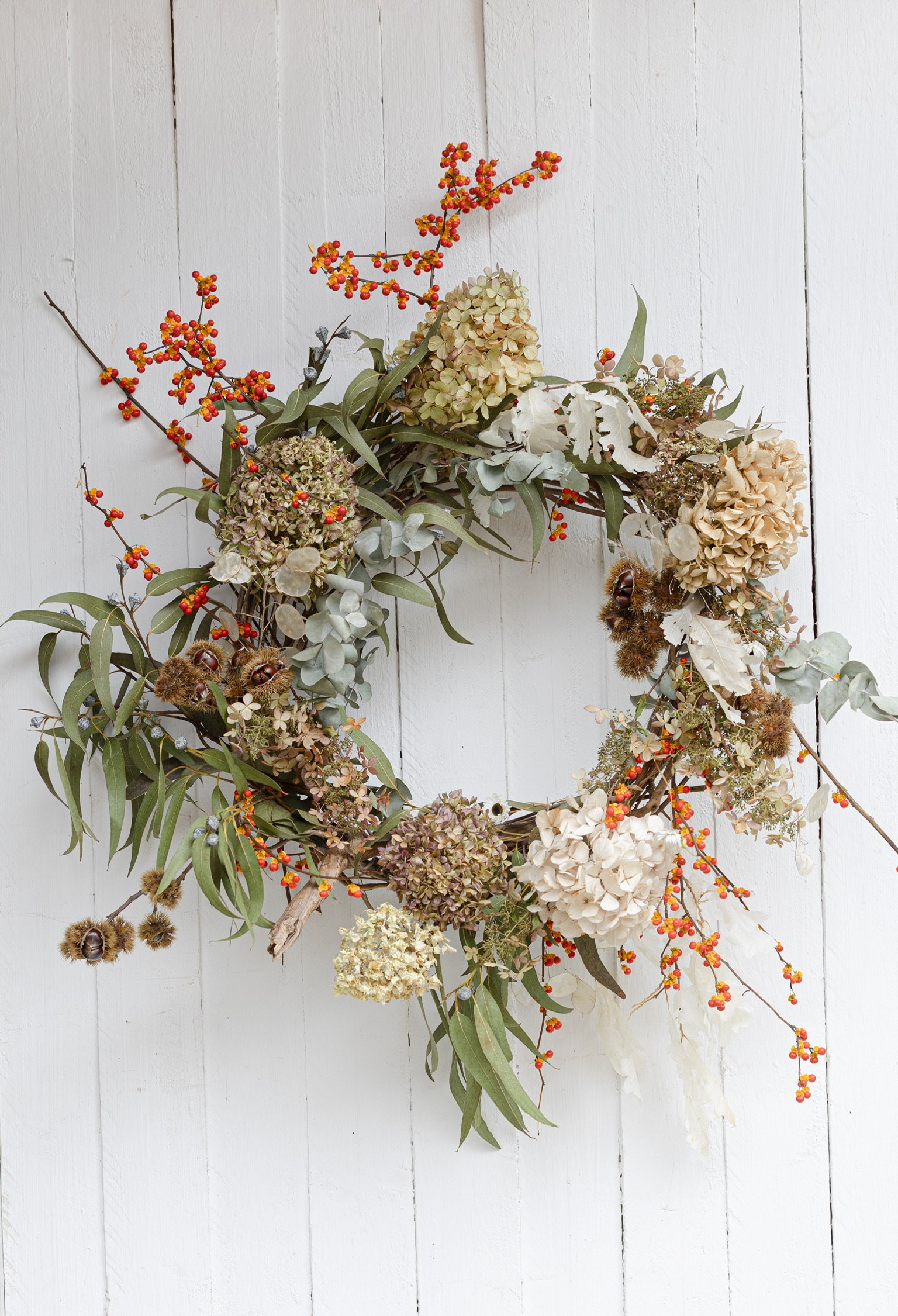 Blumenkranz mit Hortensien, Eukalyptus, Beeren und getrockneten Pflanzen, an weißen Wand