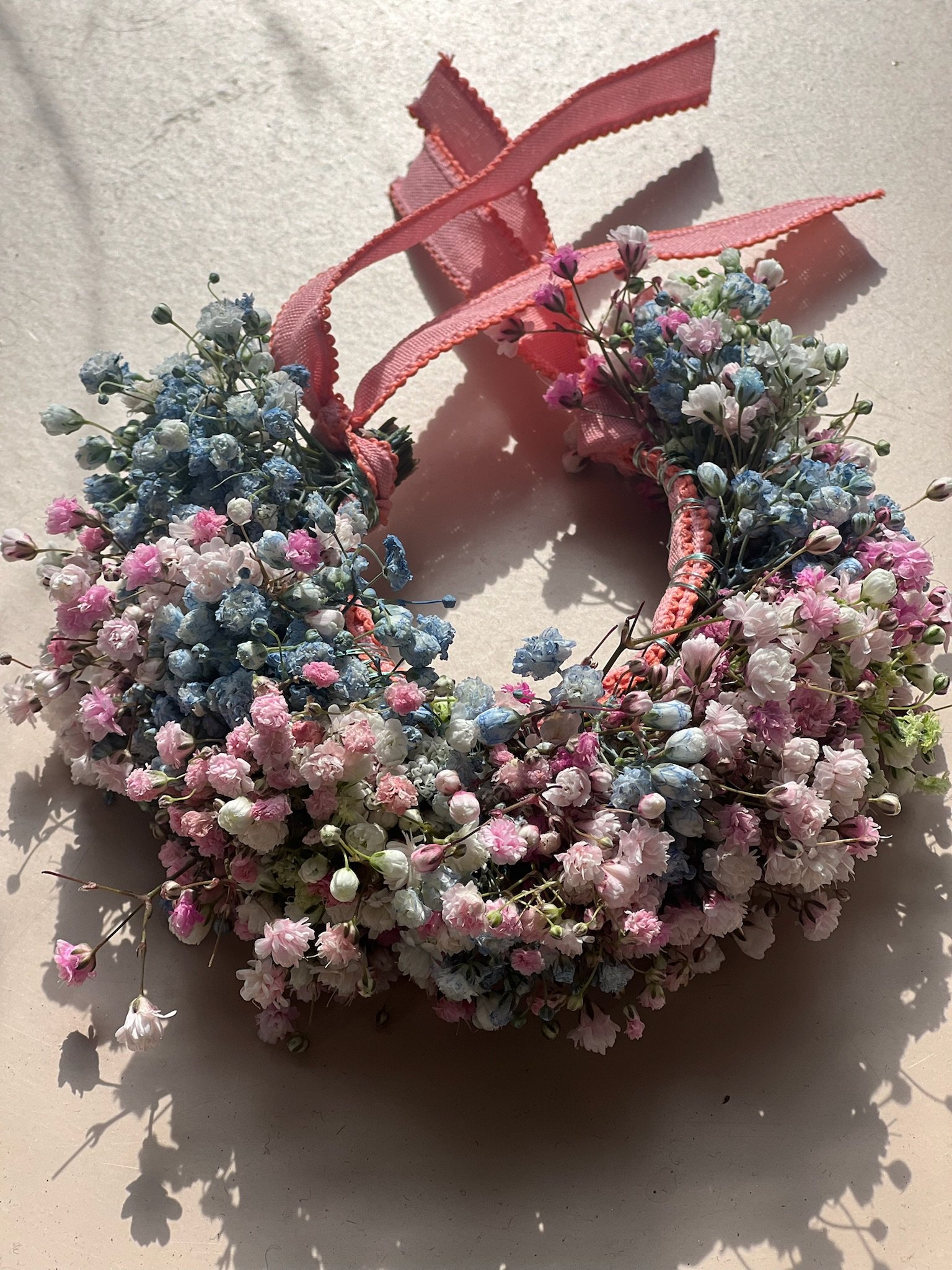 Blumenkranz aus kleinen pink, weißen und blauen Blumen mit rosa Schleifen