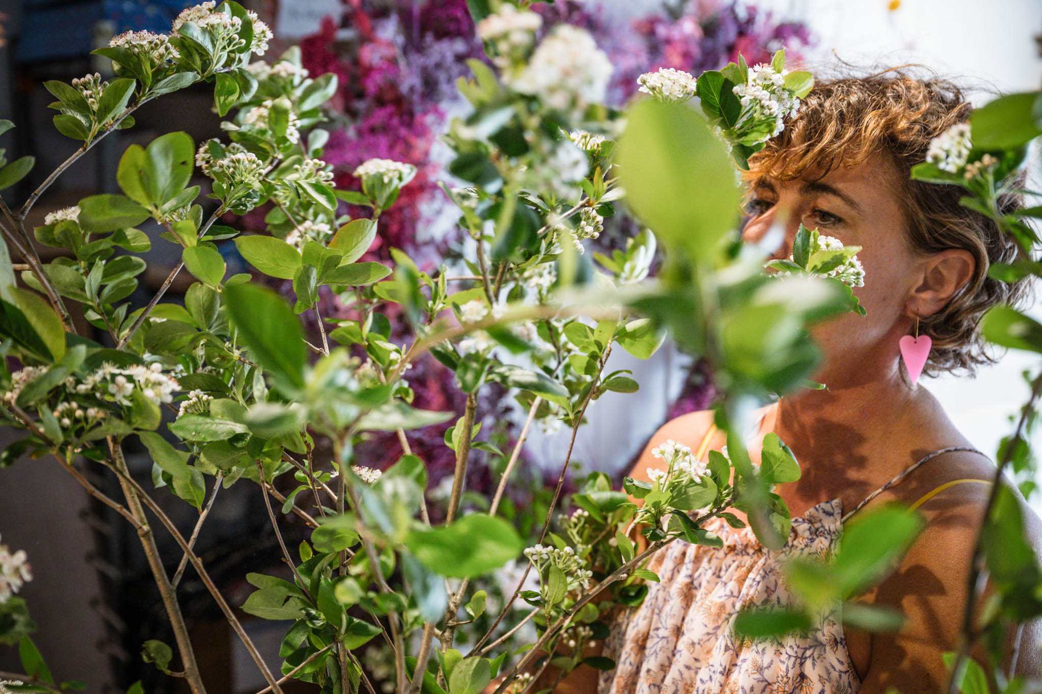 Frau mit pinker Herzohrring, die unter grünem Pflanzen- und Blumenbündel blickt.