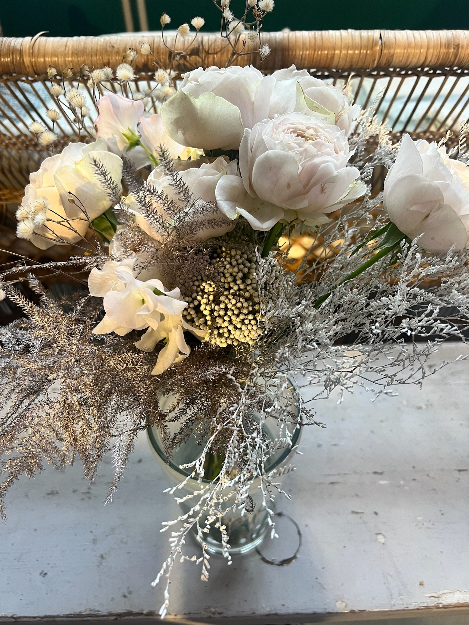 Weiße und cremefarbene Blumen in einer Vase, dazu silberne und hellbraune Dekorationen auf einem weißen Tisch.