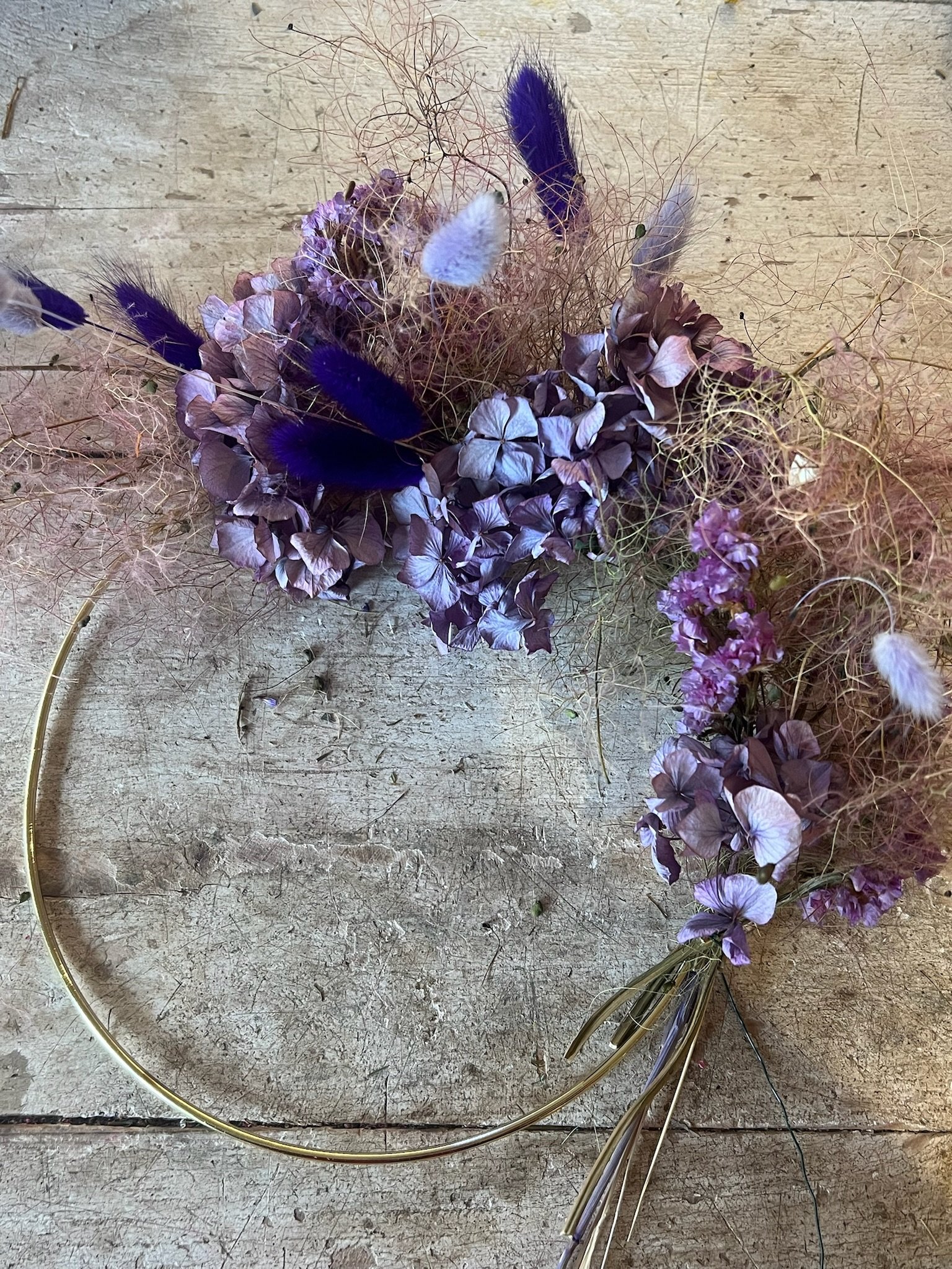 Blumenkranz aus lilafarbenen Hortensien, bunten Federn und getrockneten Pflanzen auf Holztisch