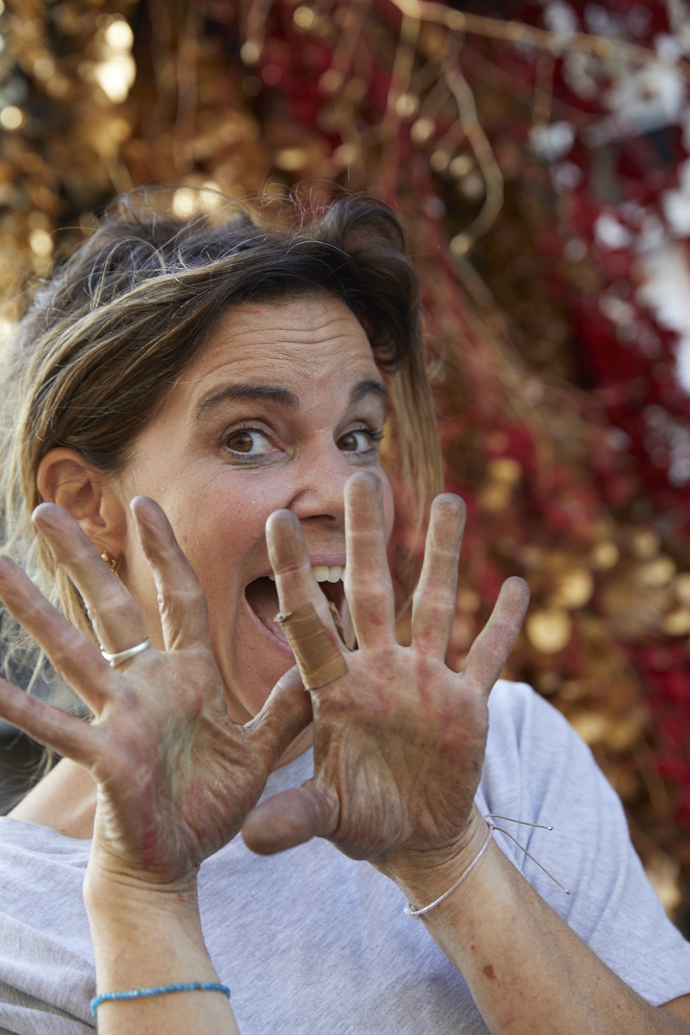 Eine Frau mit lachendem Gesicht und sichtbaren, schmutzigen Händen zeigt die Handflächen zur Kamera.