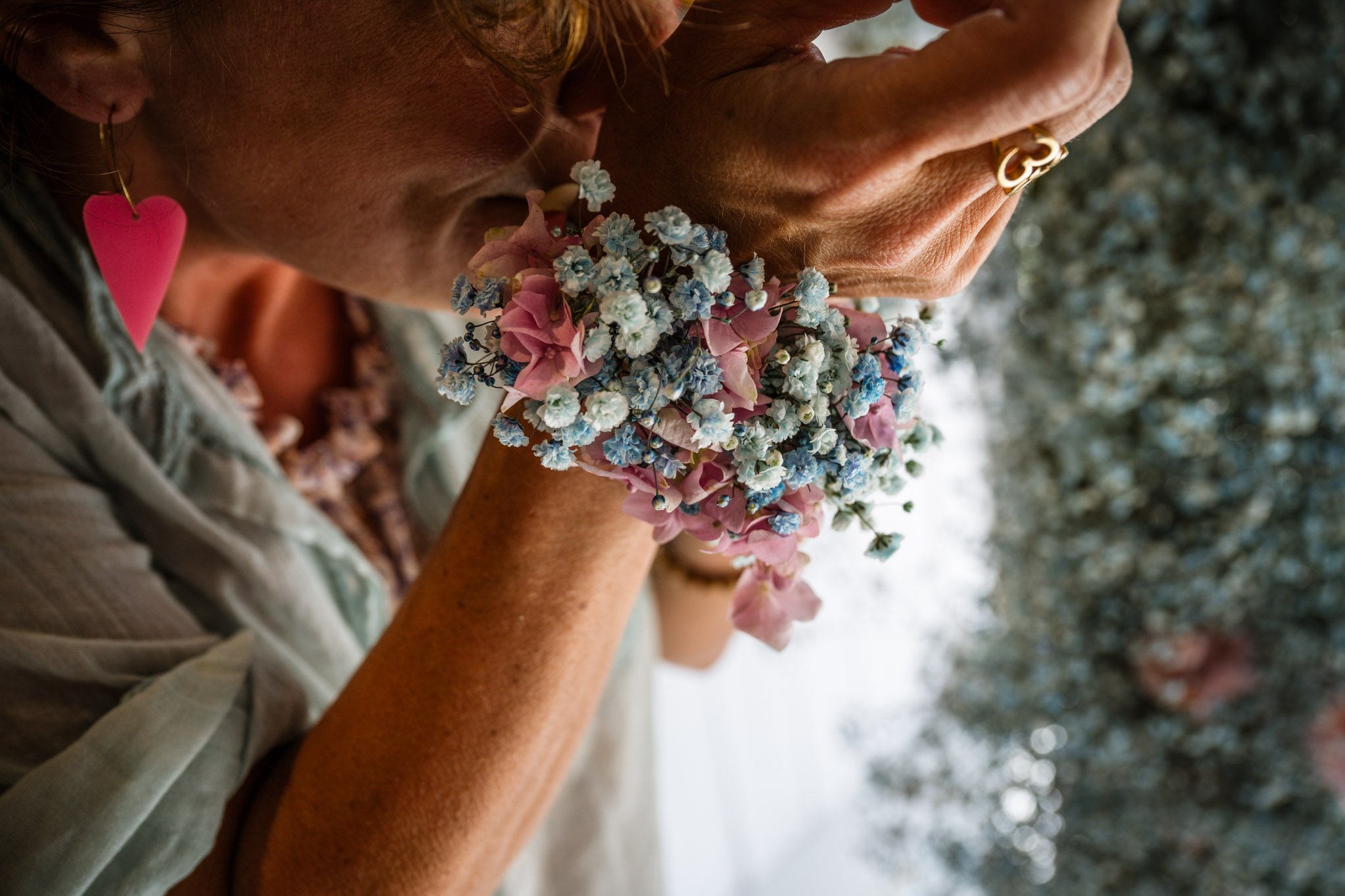 Nahaufnahme einer Person mit Blumen am Handgelenk, die den Kopf gesenkt hat, während sie betet oder meditiert, mit einem pinken Herz-Ohrring.