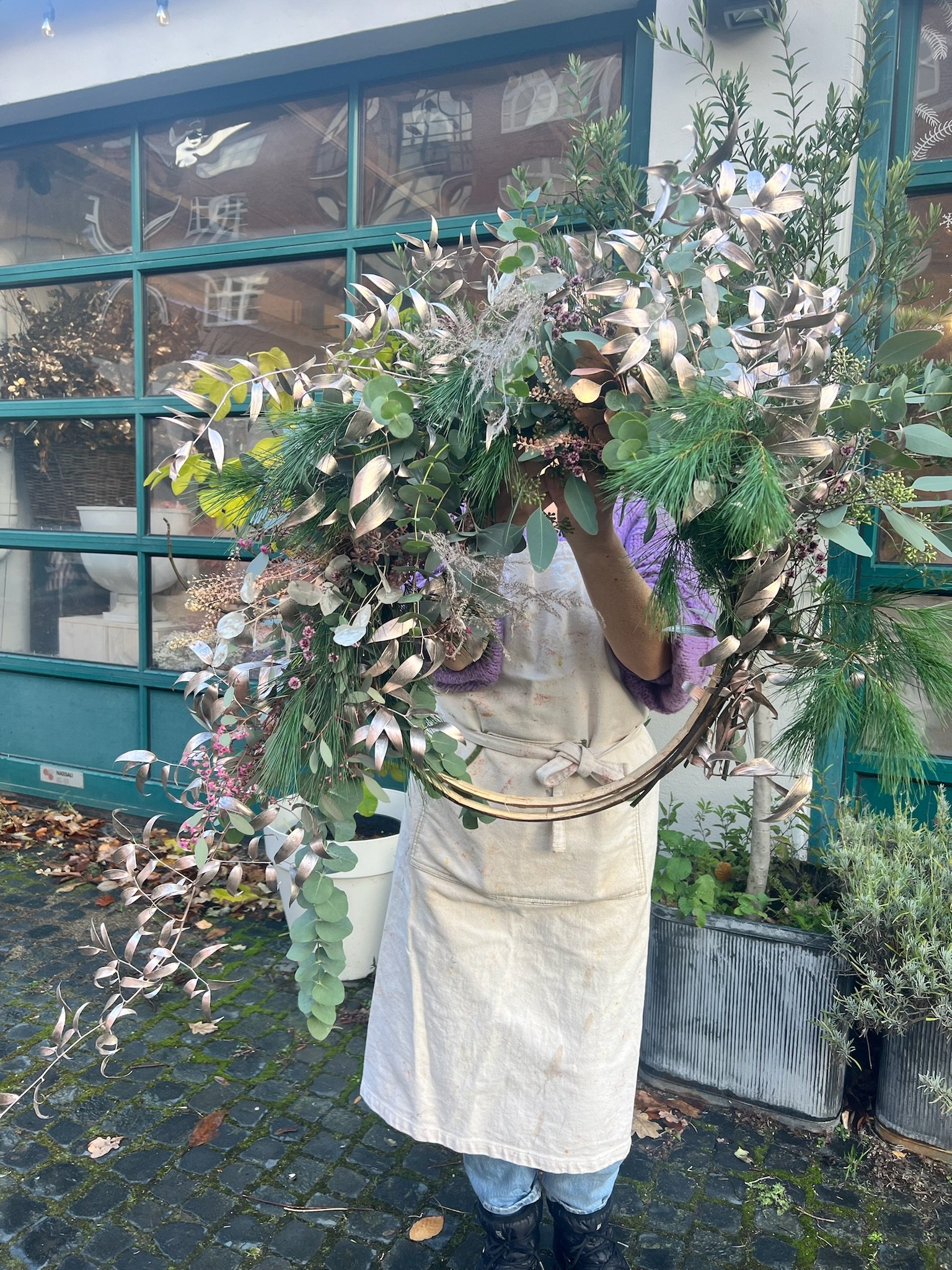 Person trägt einen großen Blumenstrauß oder eine Blumenarrangement vor einem Geschäft oder Gebäude im Freien.