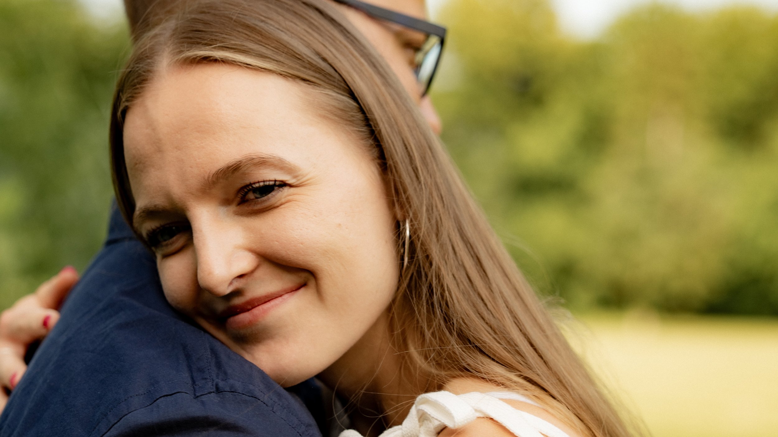 Junge Frau lächelt beim Umarmen im Freien an einem sonnigen Tag.
