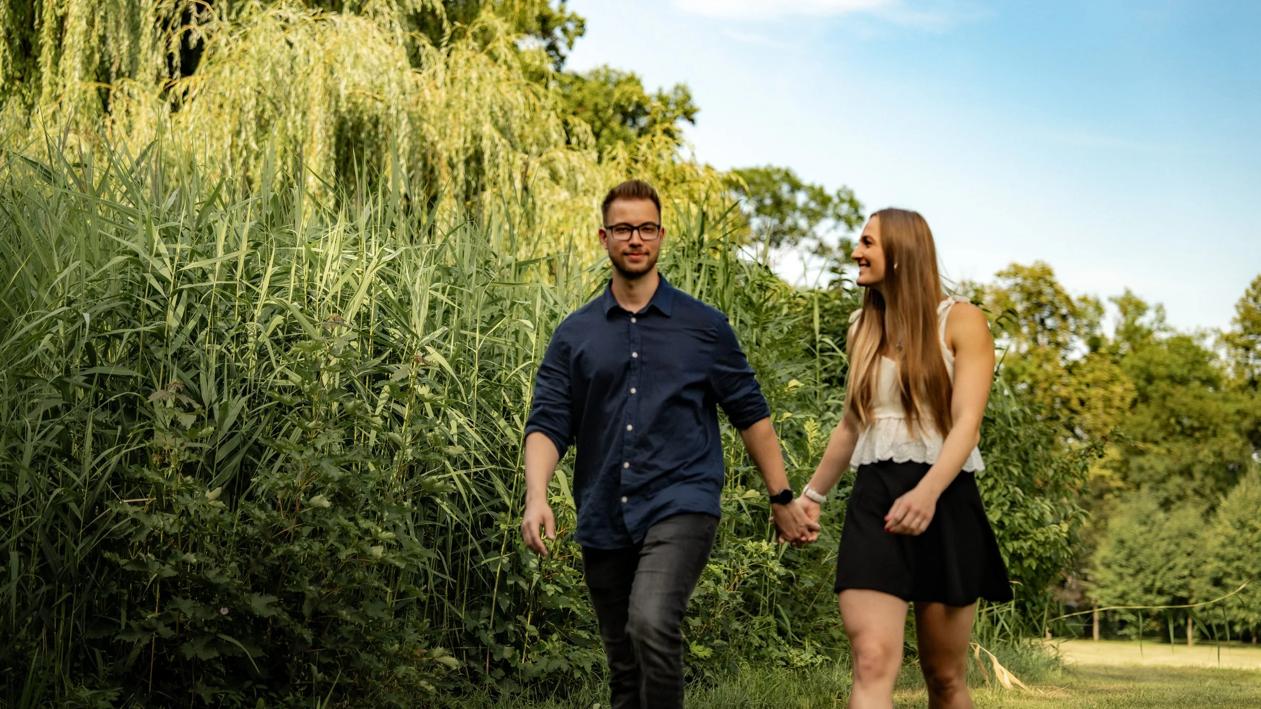 Ein Mann und eine Frau halten Händchen beim Spaziergang in einem Park an einem sonnigen Tag.