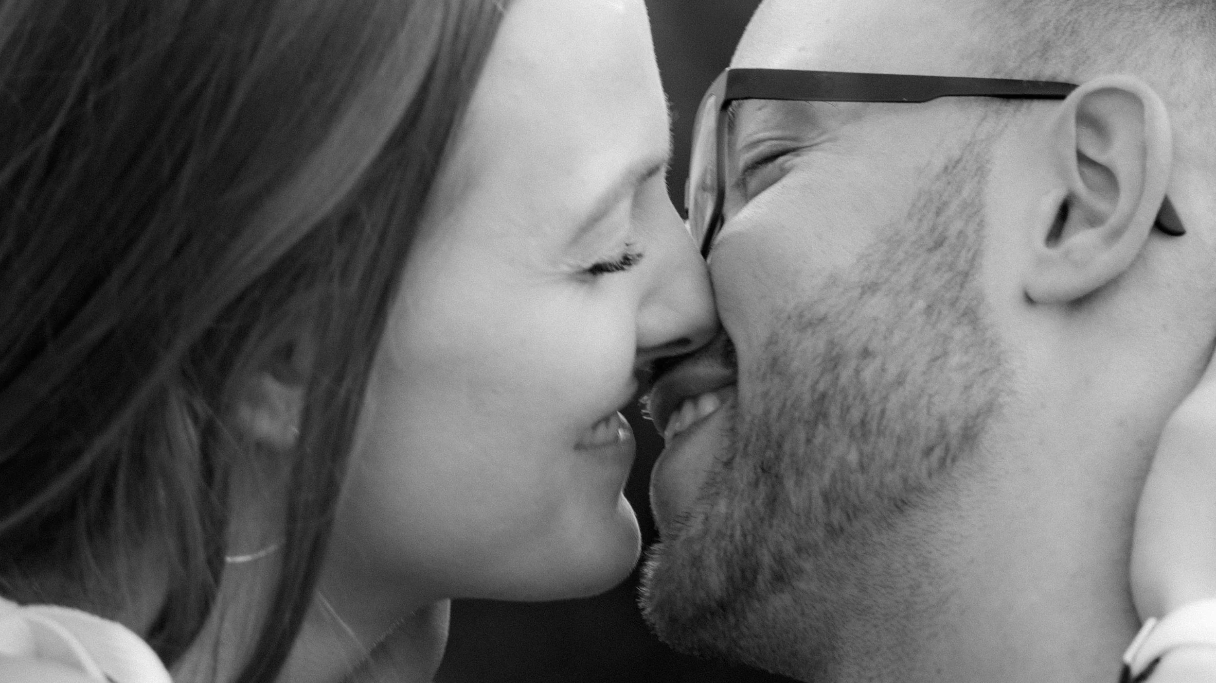 Zwei Menschen, eine Frau und ein Mann, die sich mit den Nasen berühren, lächelnd und sich nahe stehen, schwarz-weiß Foto.